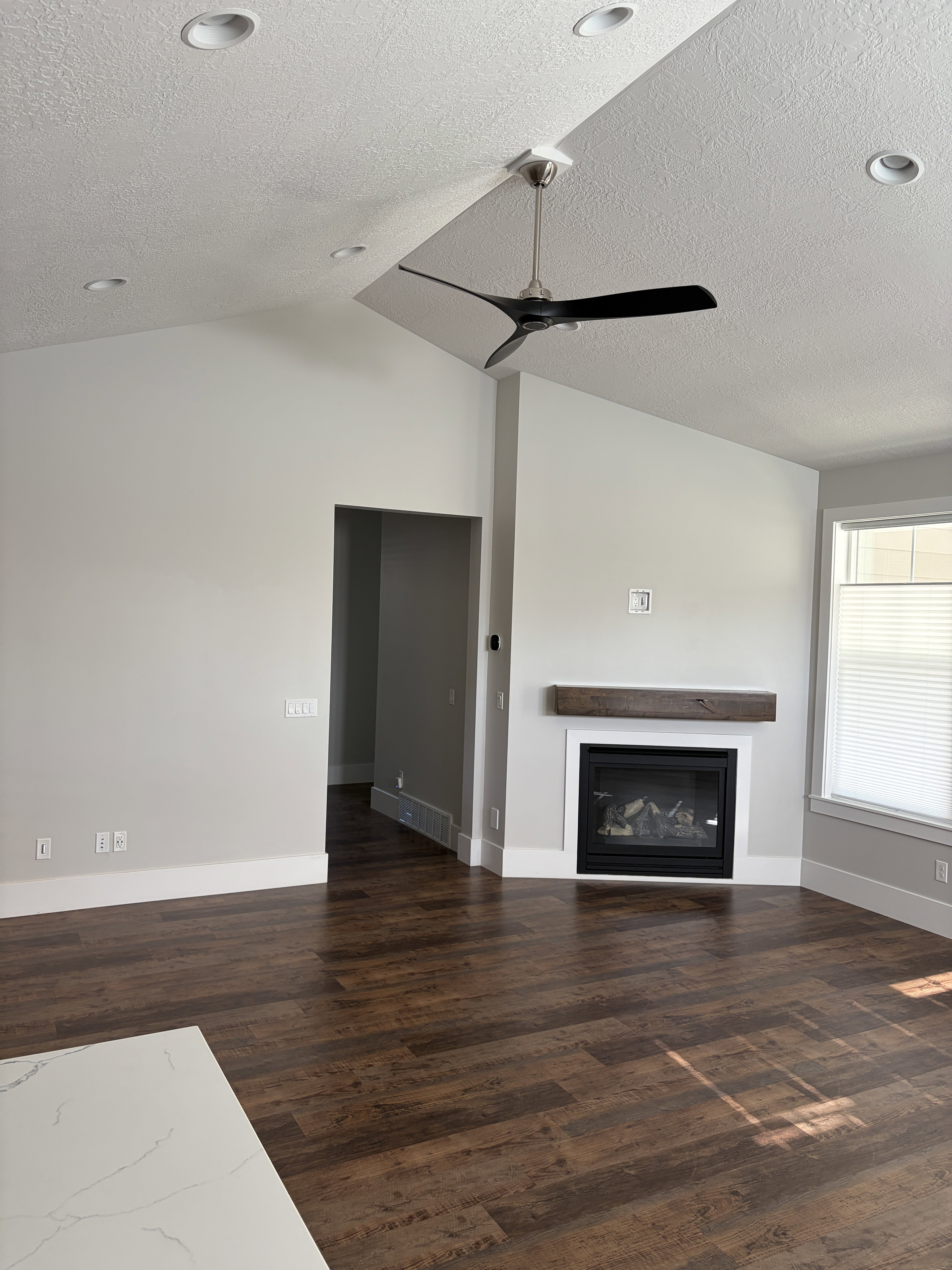 Spacious interior featuring vaulted ceilings, recessed lighting, wood-finish flooring, a contemporary ceiling fan, and a fireplace with a wood mantle