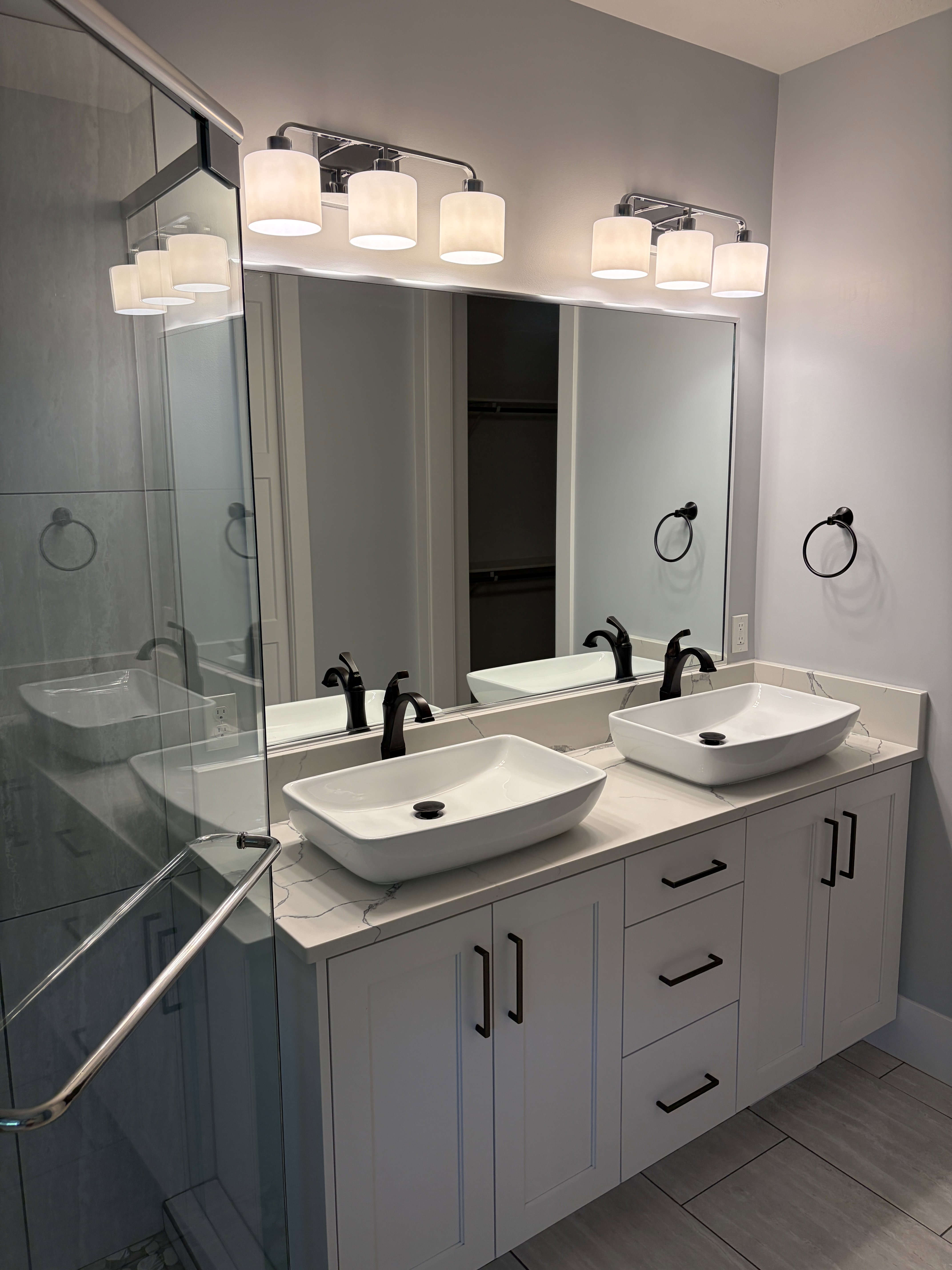 Double vanity featuring white shaker-style cabinetry with matte black hardware, dual rectangular vessel sinks with matte black faucets, and a light-toned countertop with veining