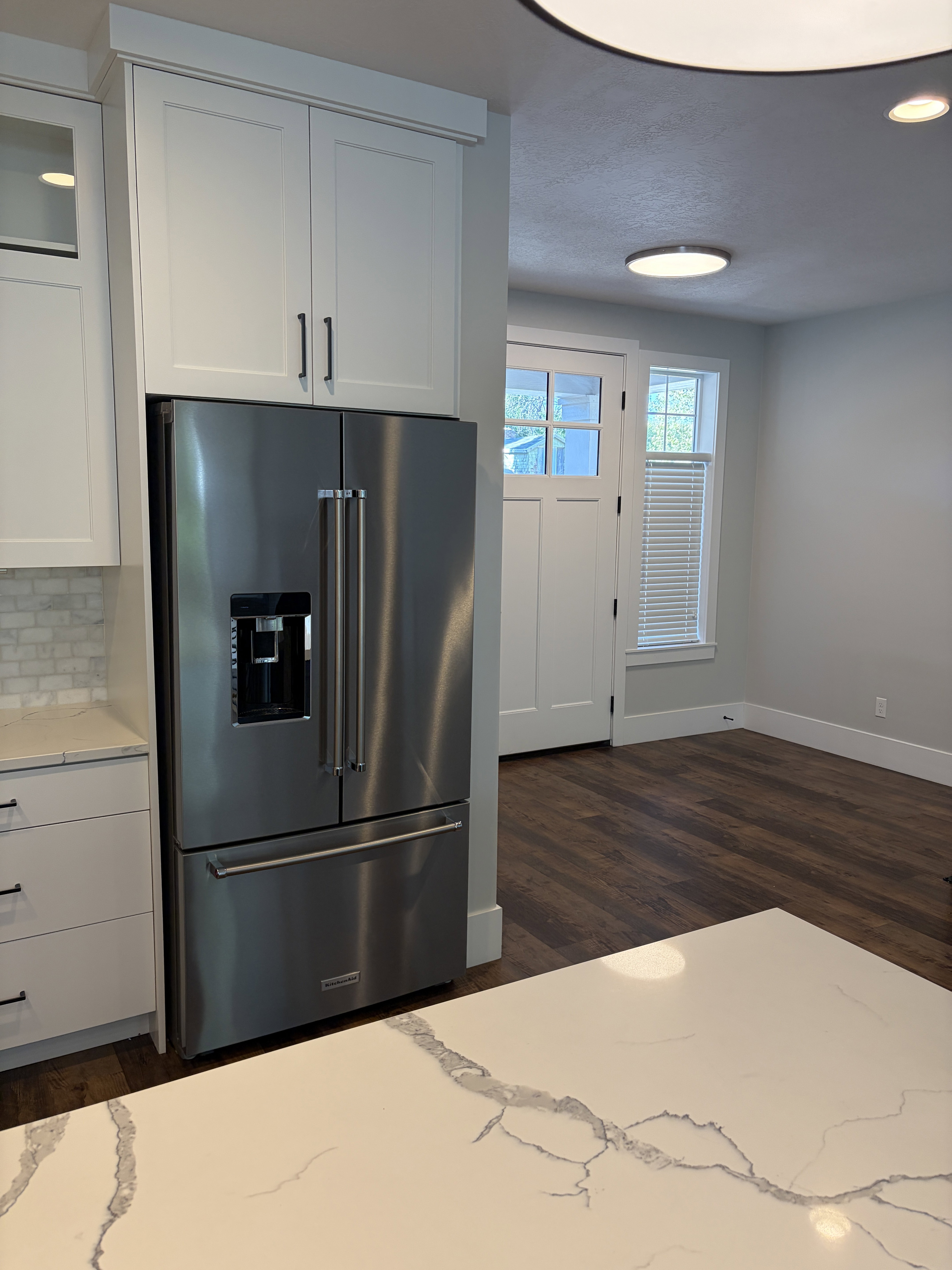 Kitchen featuring a stainless steel French door refrigerator, white shaker-style cabinetry with dark hardware, and a white countertop with gray veining