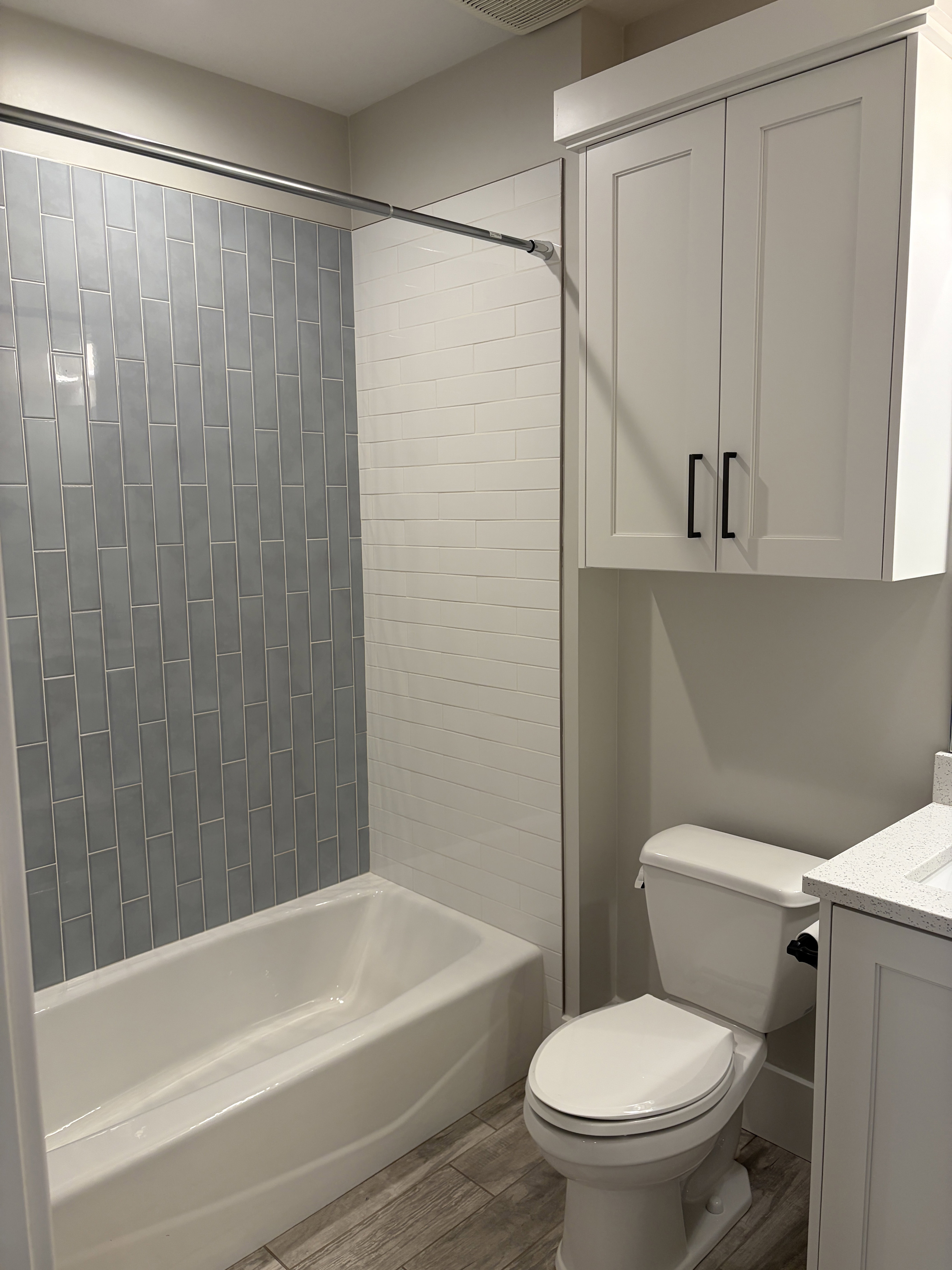 Bathroom featuring a white bathtub, blue and white subway tile shower surround, and wood-finish flooring