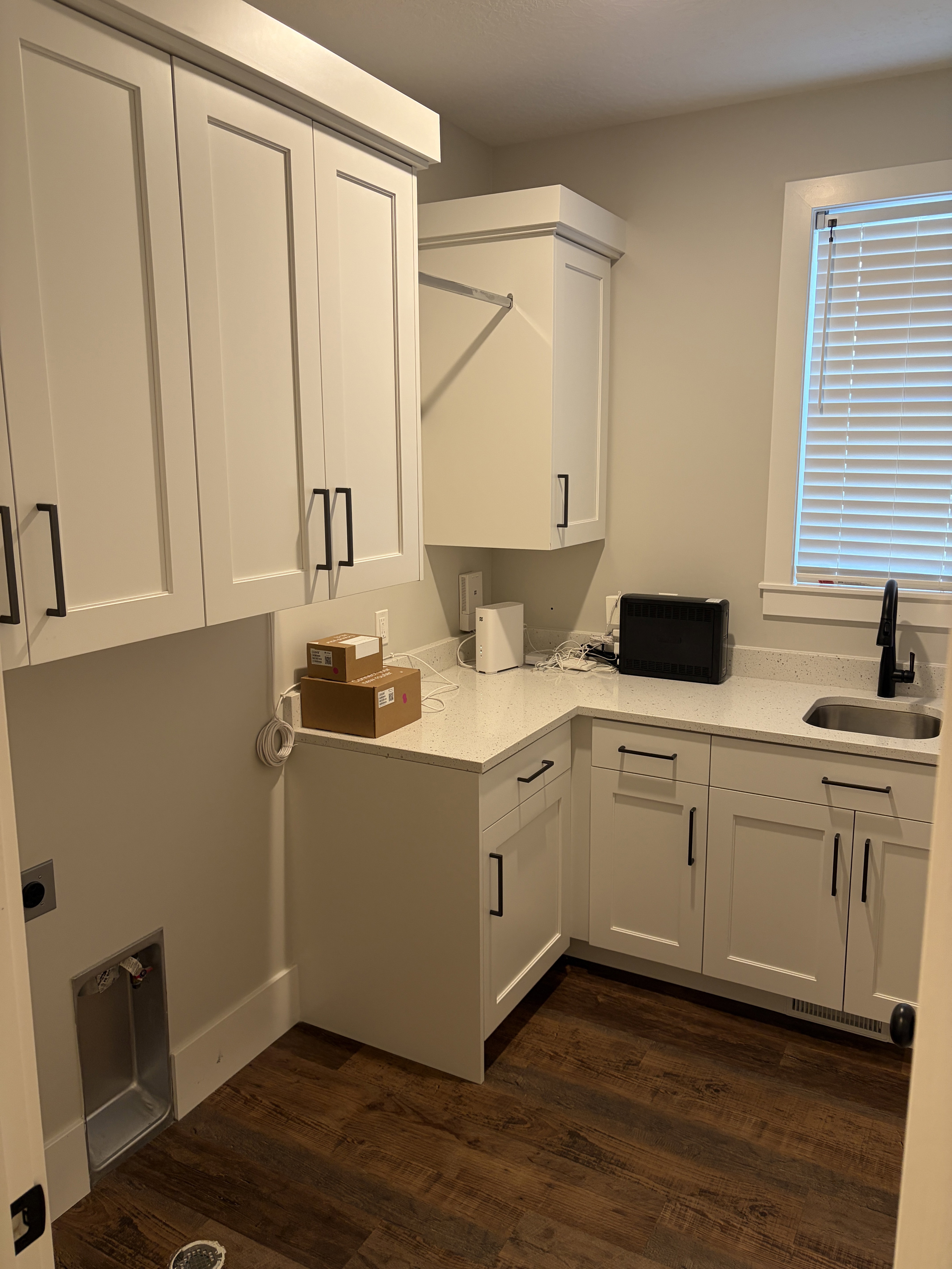 Laundry area featuring white shaker cabinetry with black hardware, an integrated sink with a black faucet, and a light-toned countertop