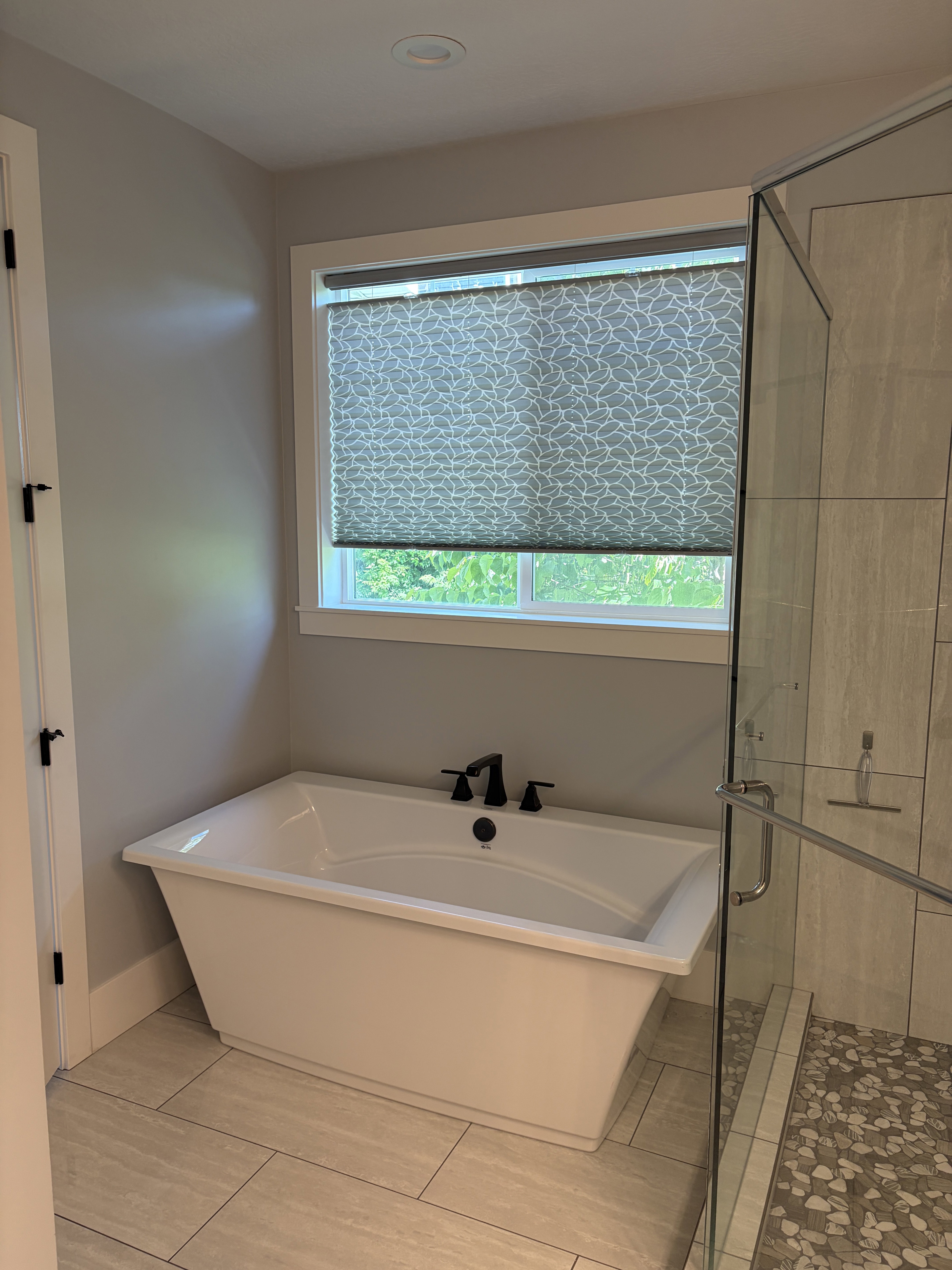 Freestanding soaking tub with matte black fixtures, set against light gray walls