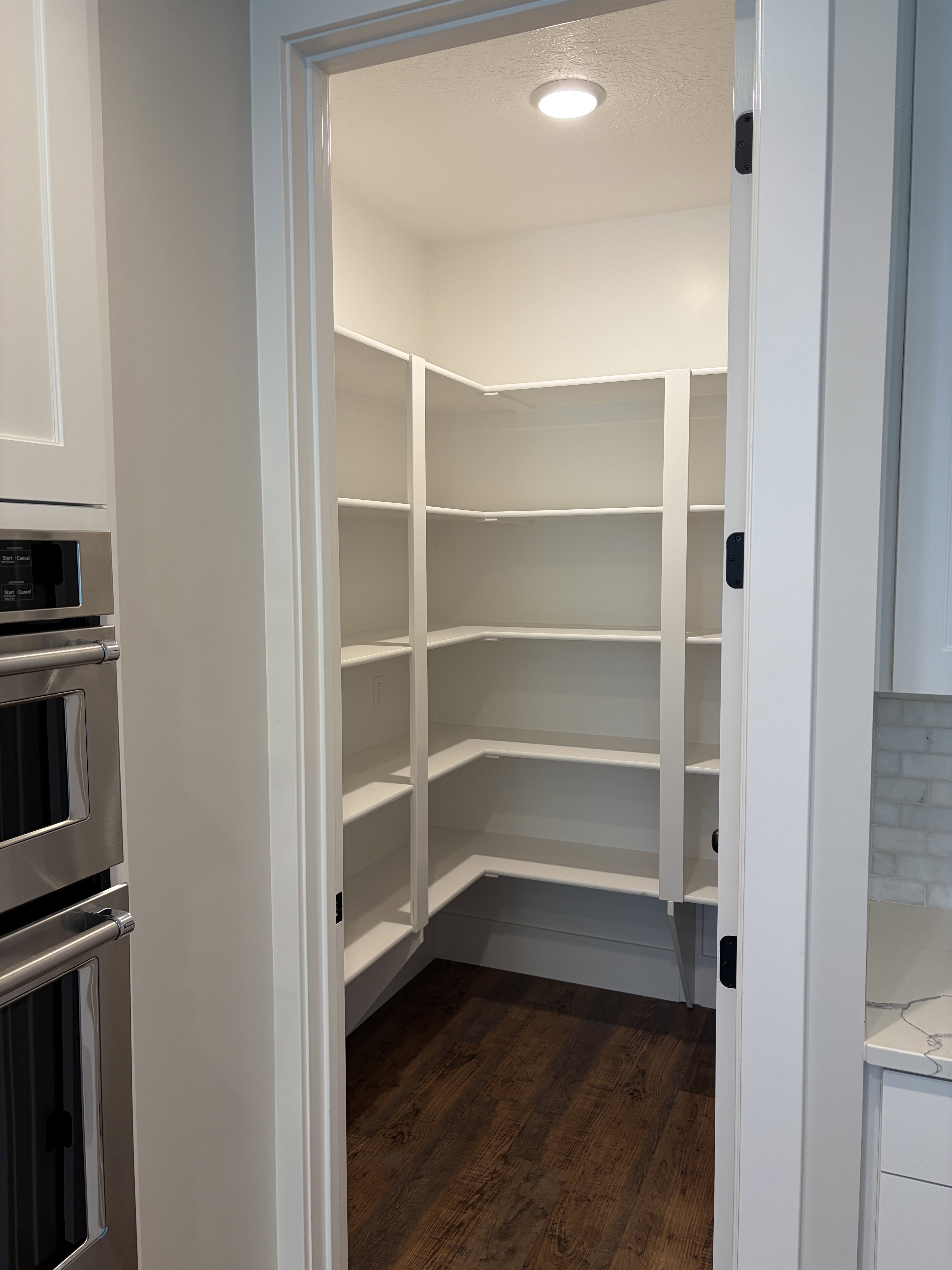 Walk-in pantry featuring extensive white built-in shelving, wood-finish flooring, and recessed ceiling lighting