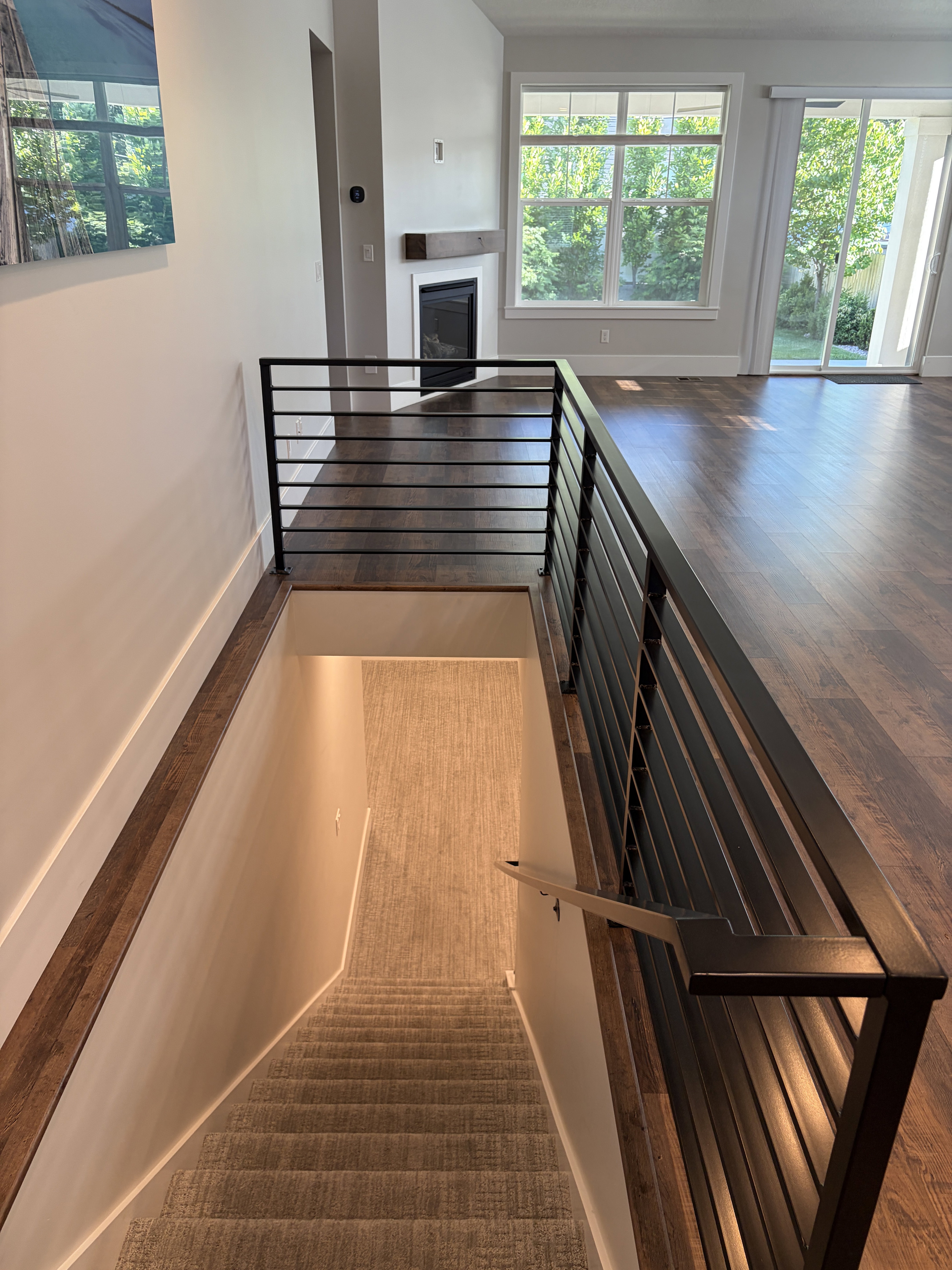 Staircase featuring contemporary horizontal metal railings leading to a carpeted lower level