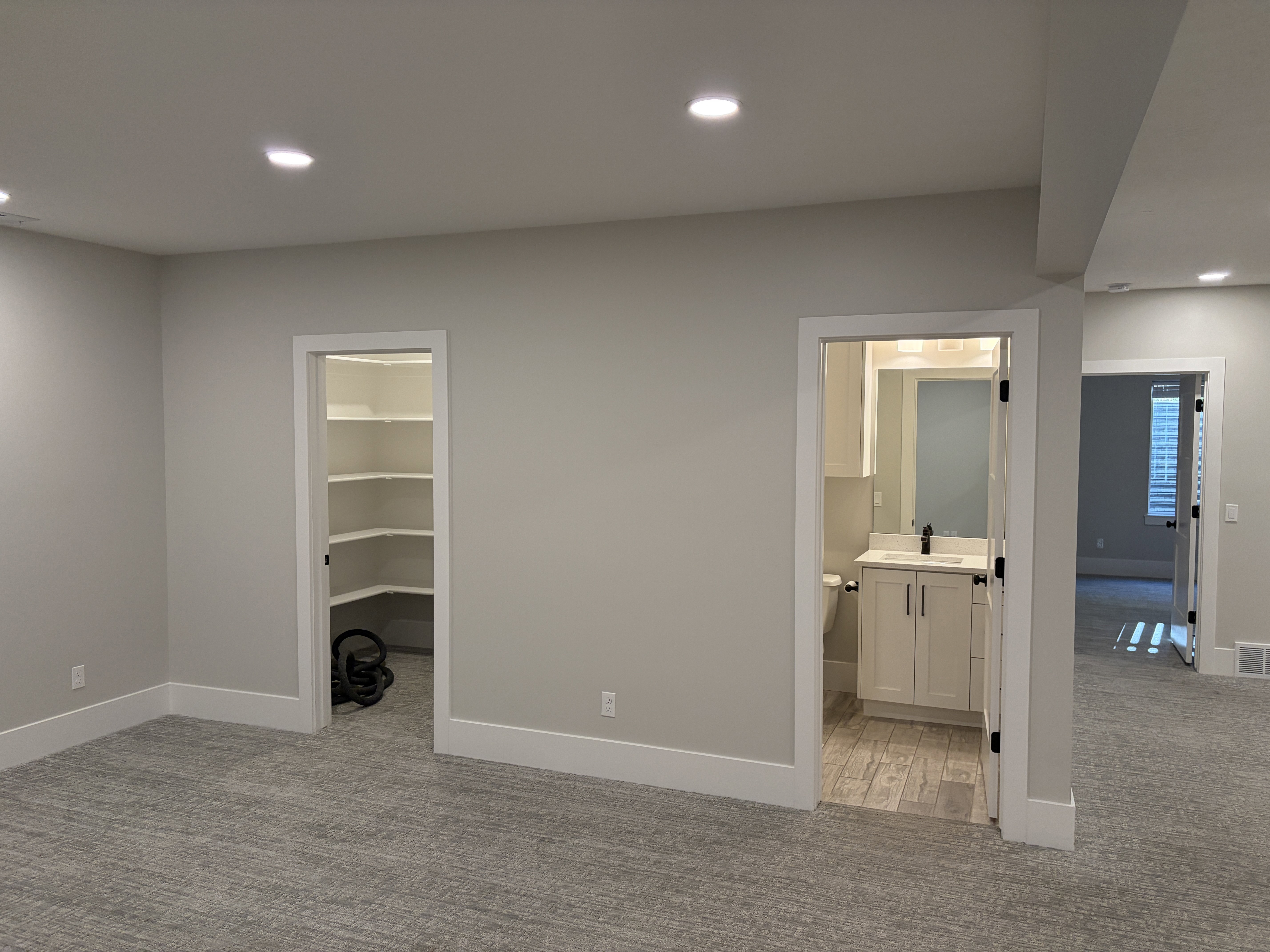 Neutral carpeting throughout, recessed ceiling lighting, a walk-in pantry with built-in shelving, and a bathroom featuring a single vanity with a black faucet, white cabinetry, and wood-look flooring