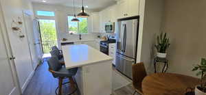 Modern kitchen featuring white shaker cabinetry, stainless steel appliances, a white countertop island with seating, and wood-finish flooring
