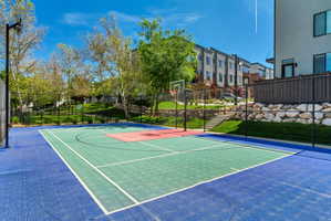 Multi-color outdoor sports court with a basketball hoop, surrounded by black chain-link fencing