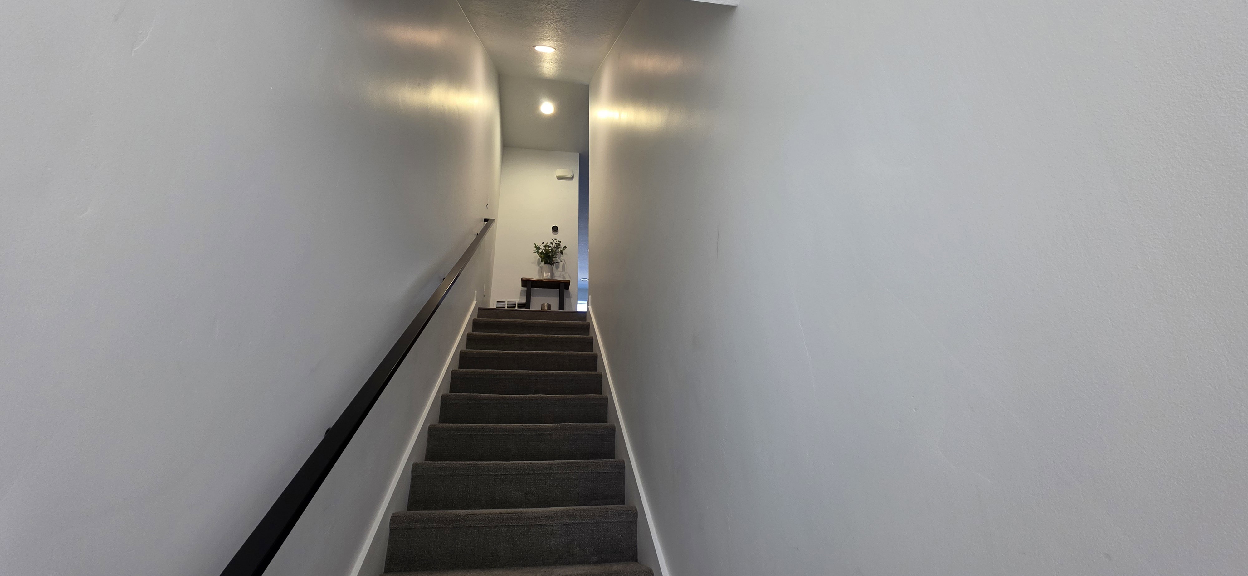 Carpeted staircase with a black handrail and recessed ceiling lighting, leading to an upper landing with a built-in console table