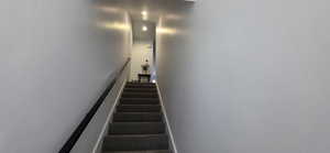 Carpeted staircase with a black handrail and recessed ceiling lighting, leading to an upper landing with a built-in console table