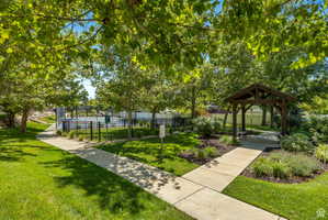Outdoor amenity space featuring a paved pathway, expansive lawn, mature shade trees, and a wooden gazebo