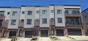 Modern townhome exteriors featuring red brick accents, light gray siding, black framed windows, and individual garage doors