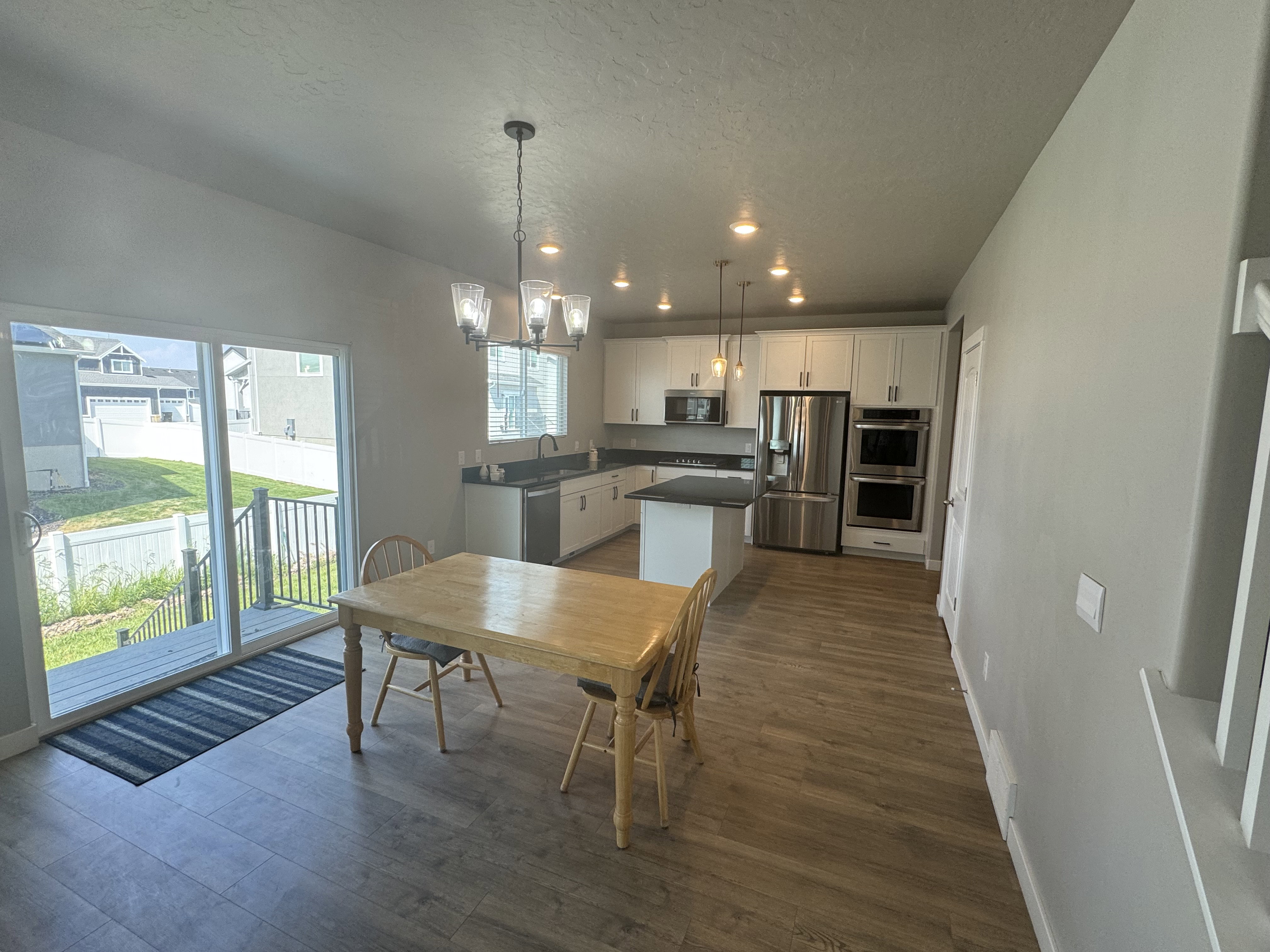 Open-concept kitchen and dining area featuring wood-finish flooring, white cabinetry, dark countertops, and stainless steel appliances