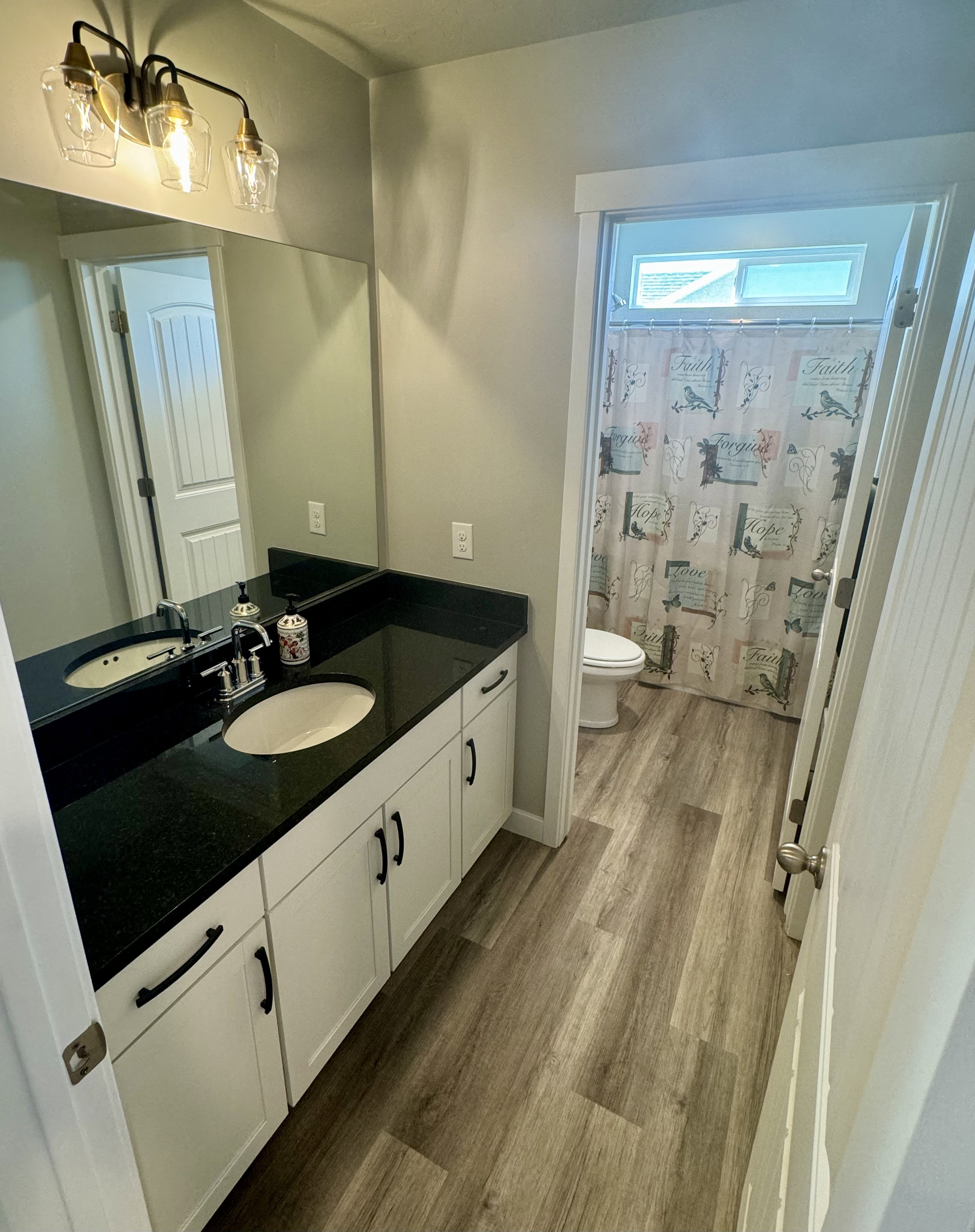 Bathroom vanity featuring dual undermount sinks, a dark countertop, and white cabinetry with black hardware