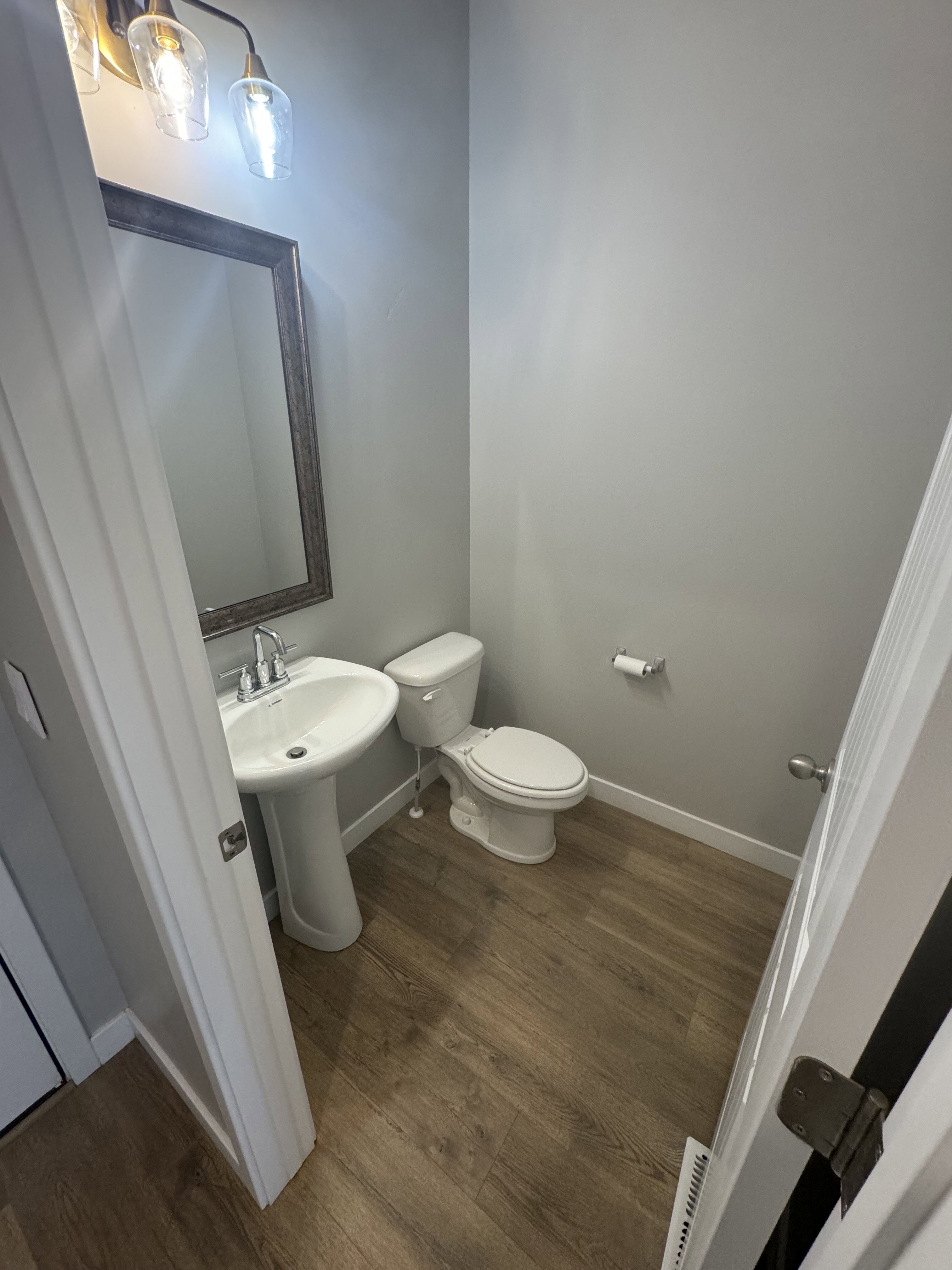 Compact powder room featuring wood-finish flooring, a white pedestal sink, and a framed mirror