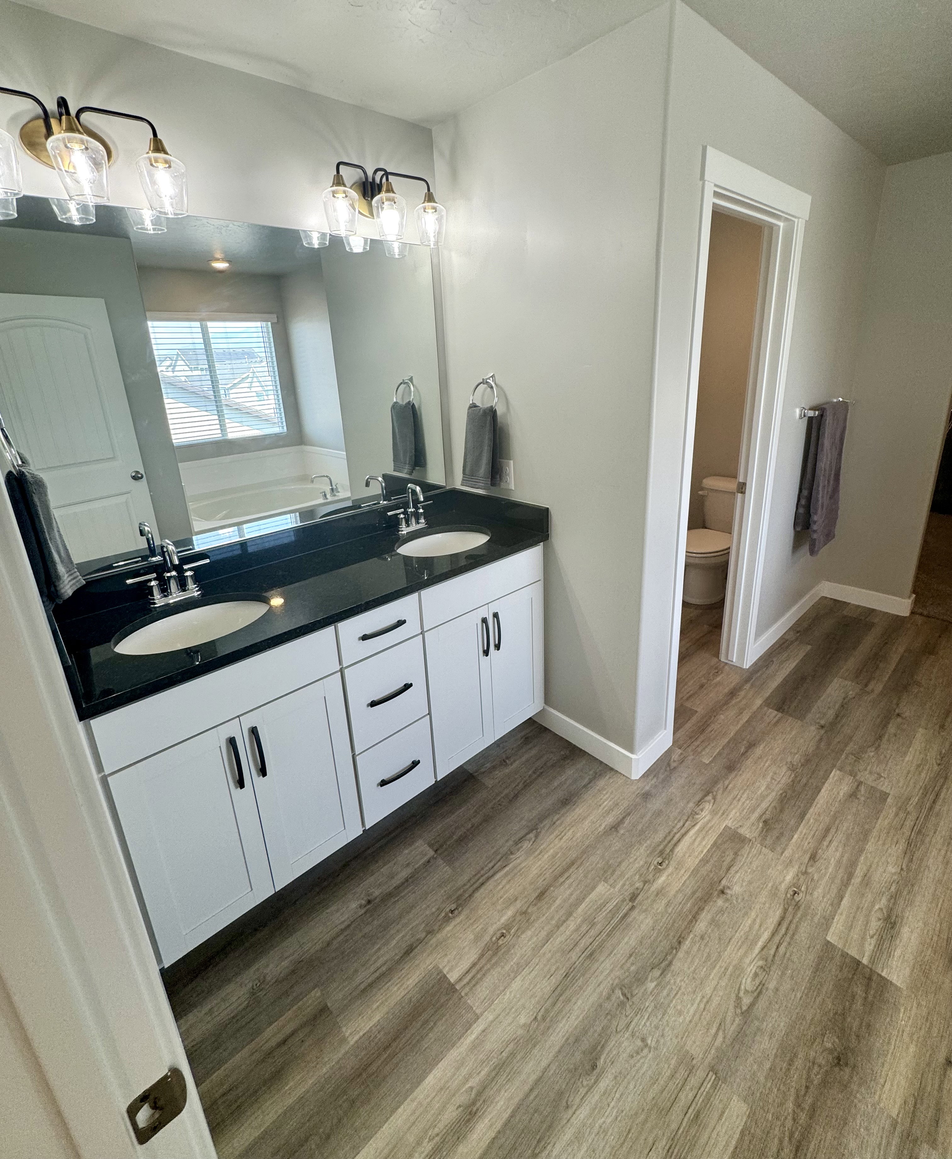 Dual vanity featuring a black countertop and white cabinetry with black hardware