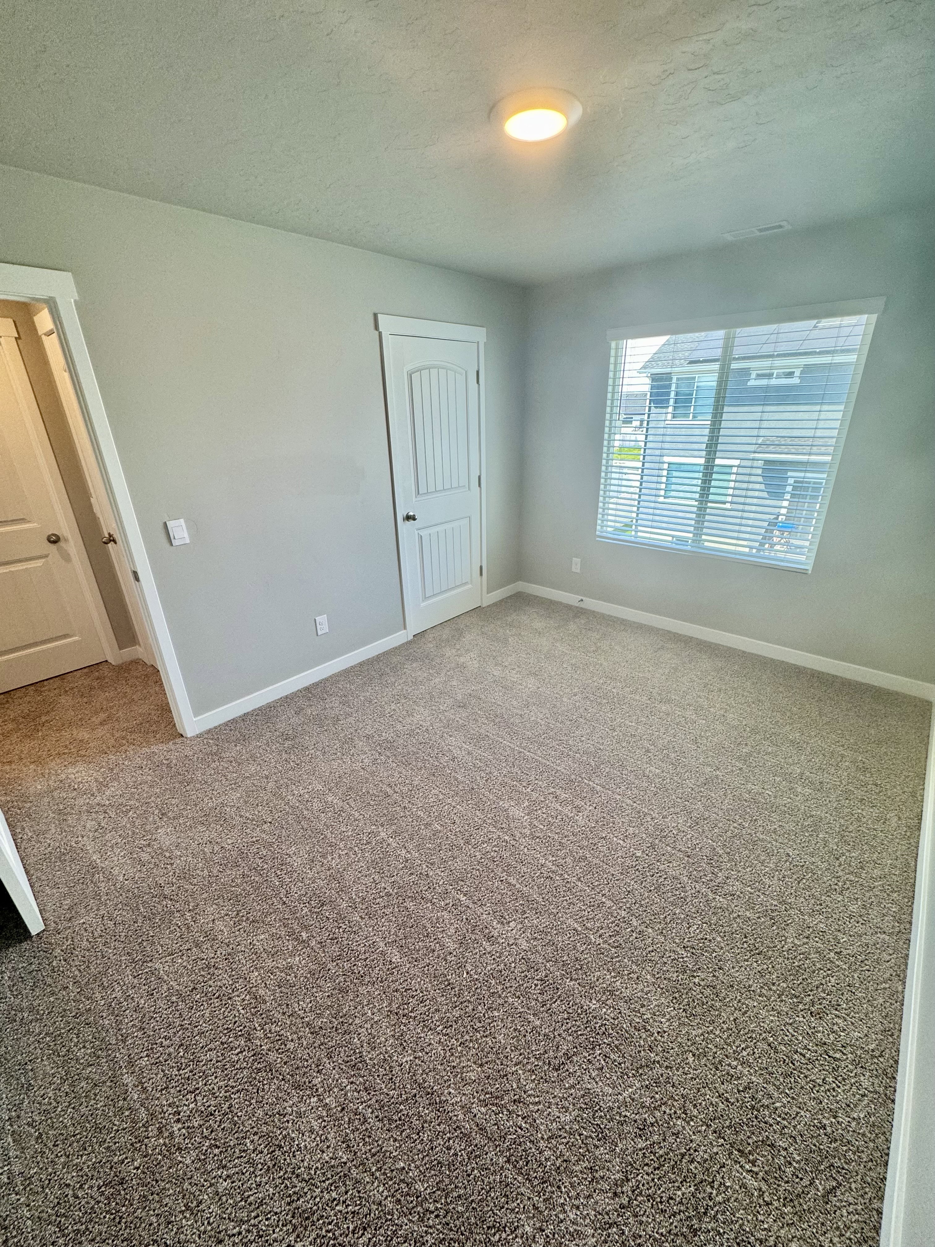 Carpeted room featuring light gray walls, a white paneled door, and a recessed ceiling light