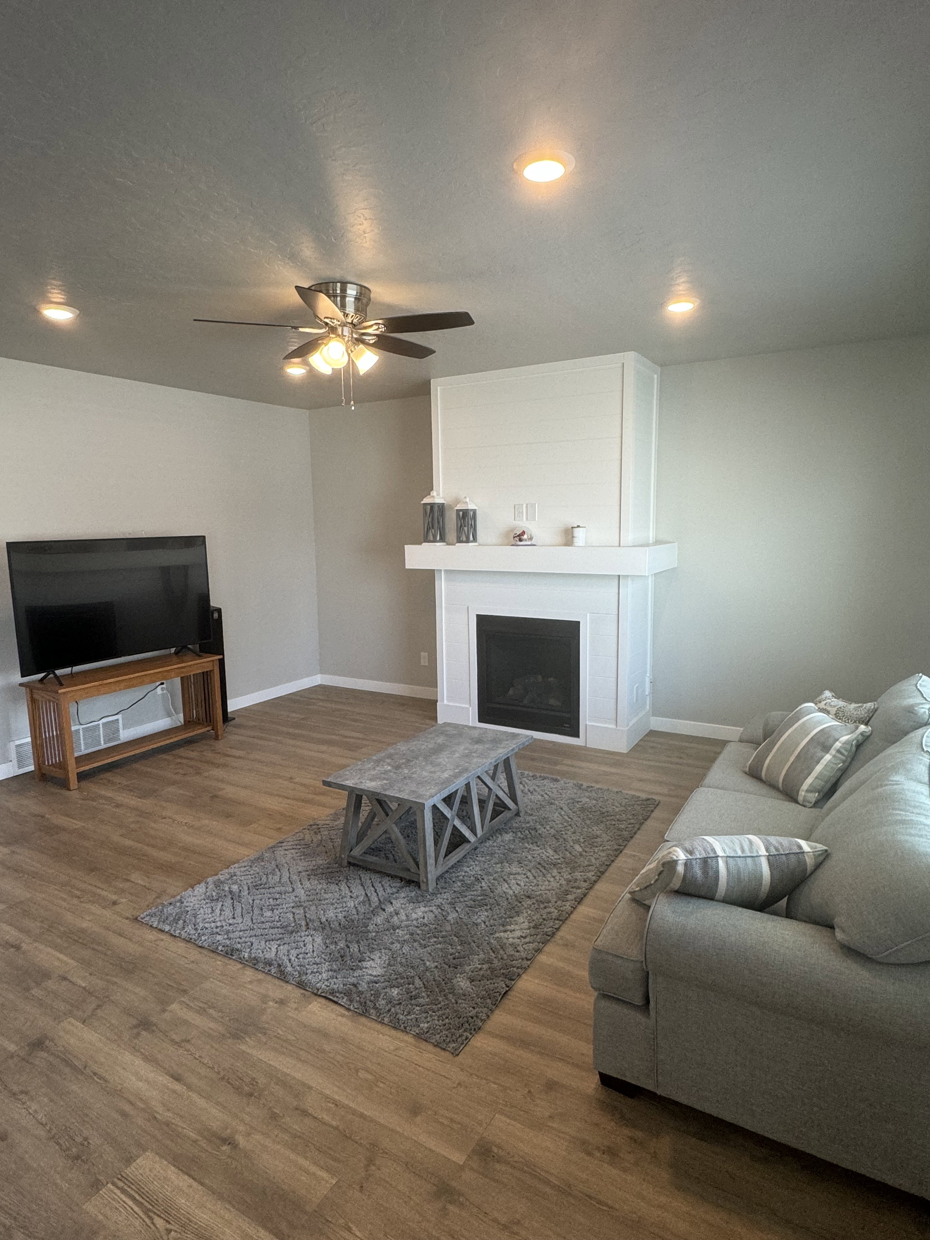 Living area featuring wood-finish flooring, a contemporary fireplace with a white mantel, and recessed ceiling lighting