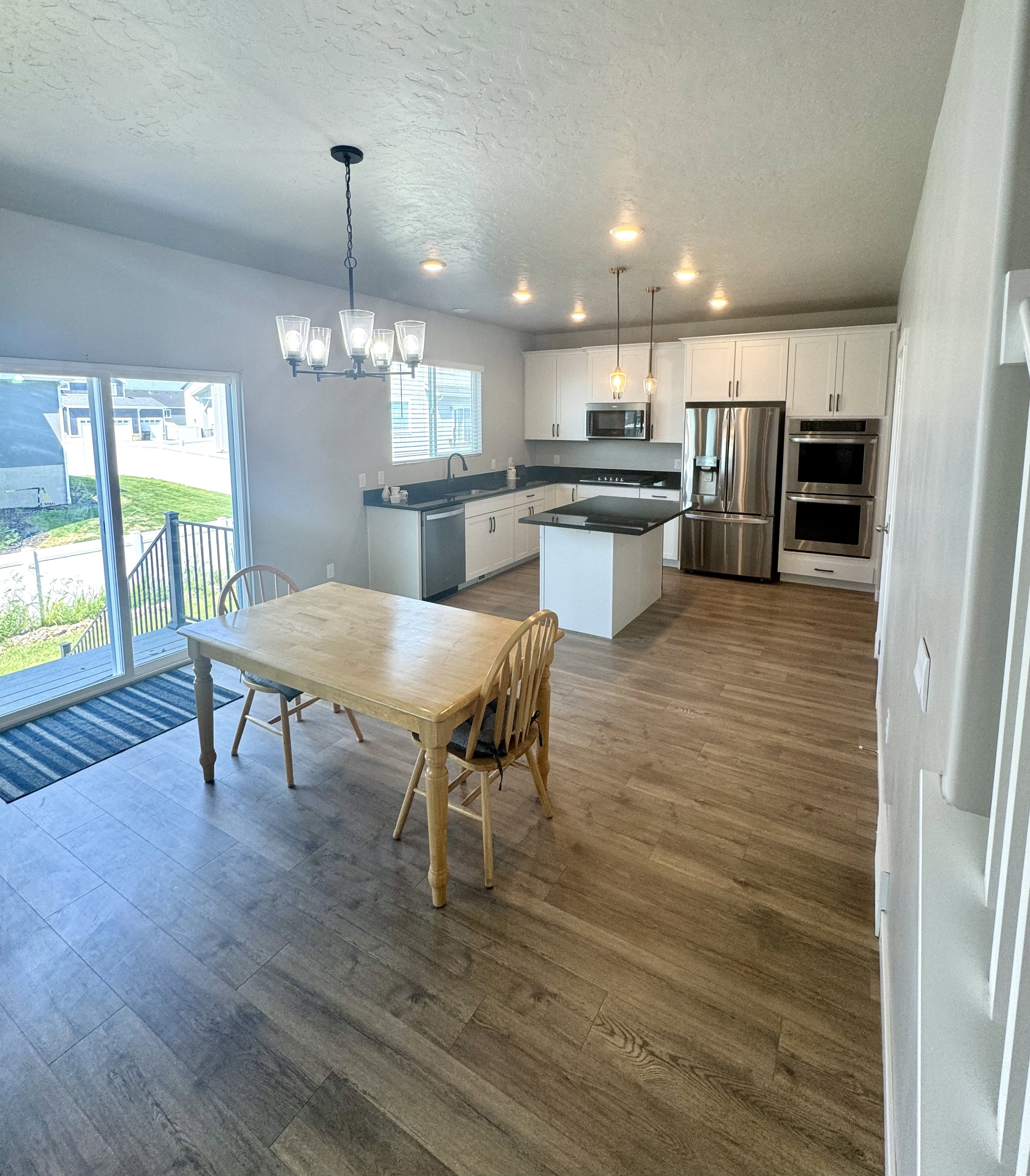 Kitchen and dining area featuring wood-finish flooring, white cabinetry, dark countertops, stainless steel appliances, and an island with pendant lighting
