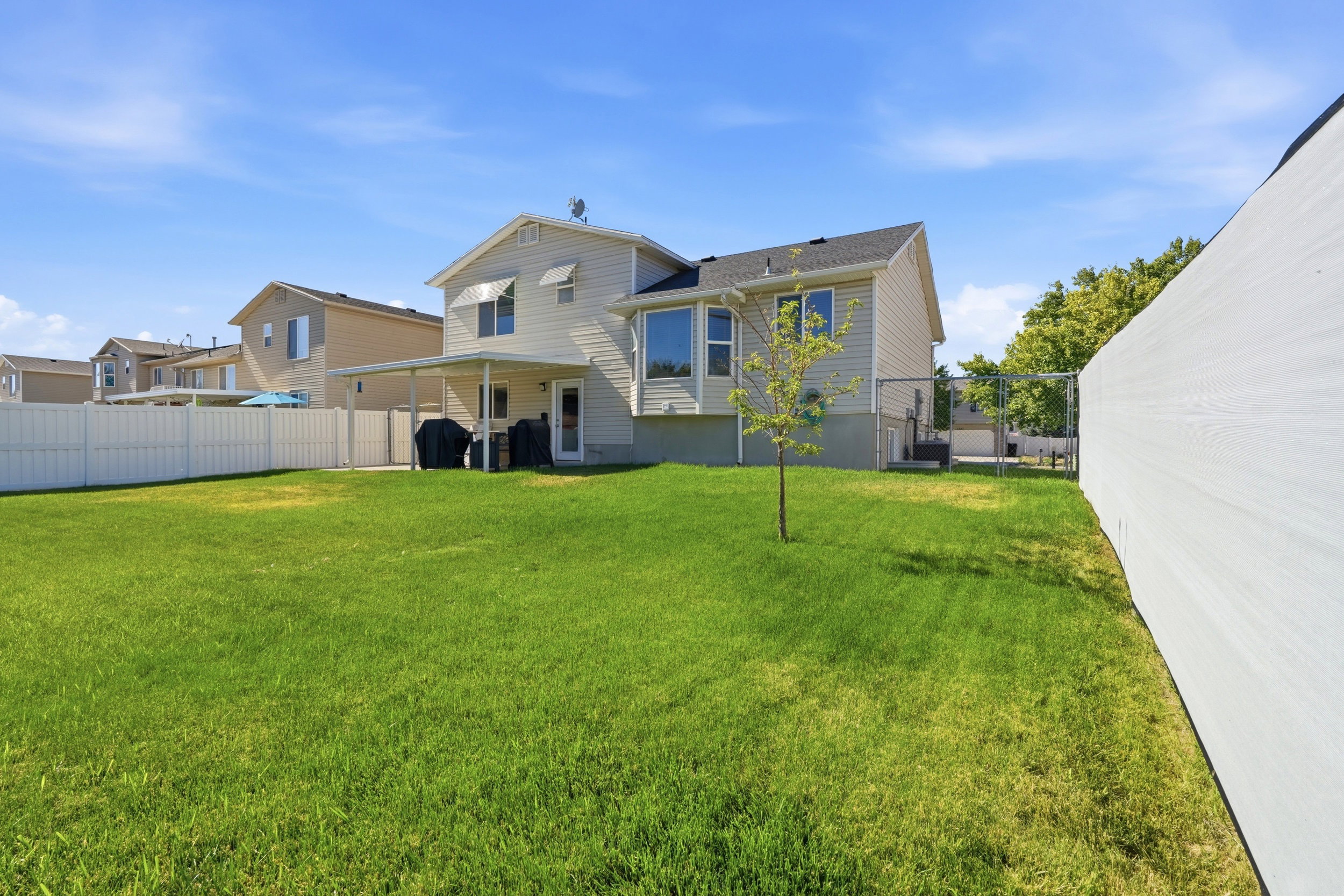 Expansive backyard featuring a lush lawn, white privacy fencing, and a covered patio area