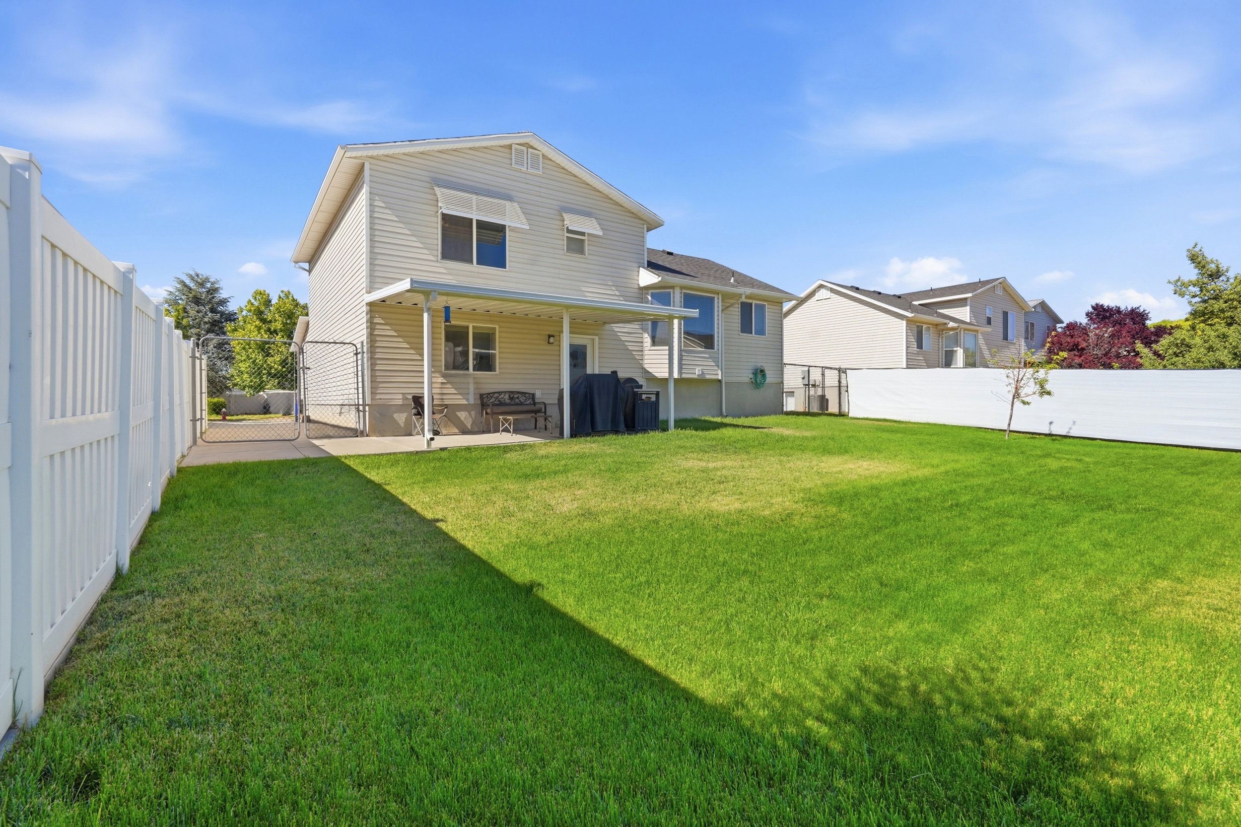 Expansive green lawn with a white vinyl fence and a covered patio