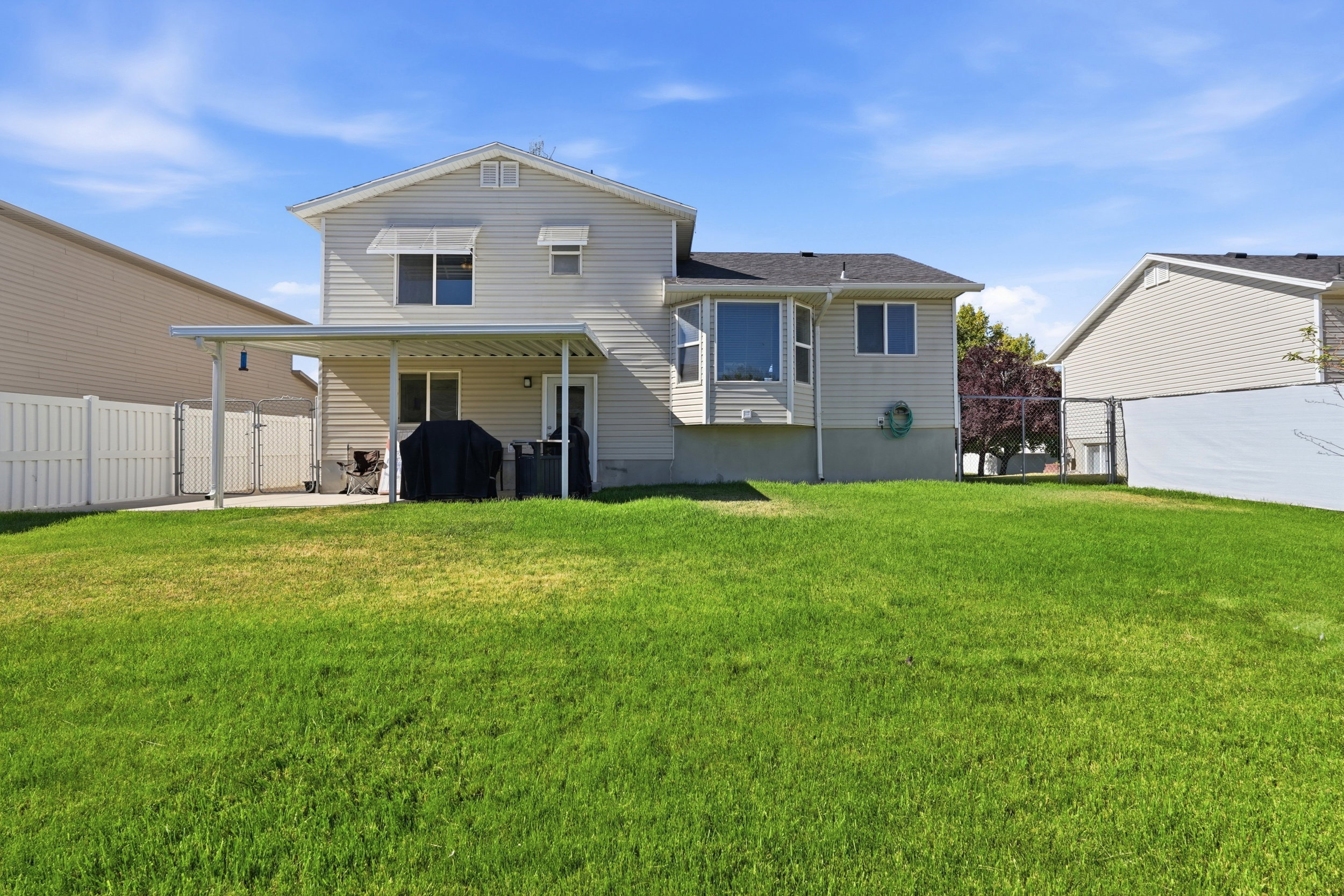Expansive green lawn extending from a covered patio structure, featuring a bay window on the rear elevation, horizontal siding, and a privacy fence