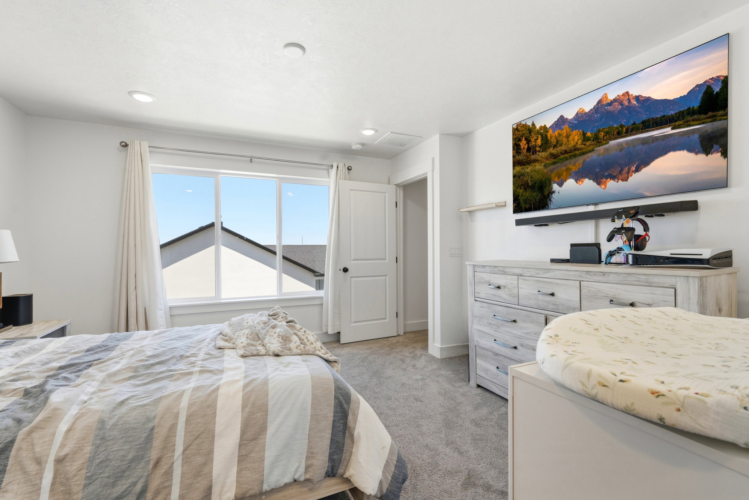 Bright bedroom featuring a large window, recessed lighting, and light gray carpeting