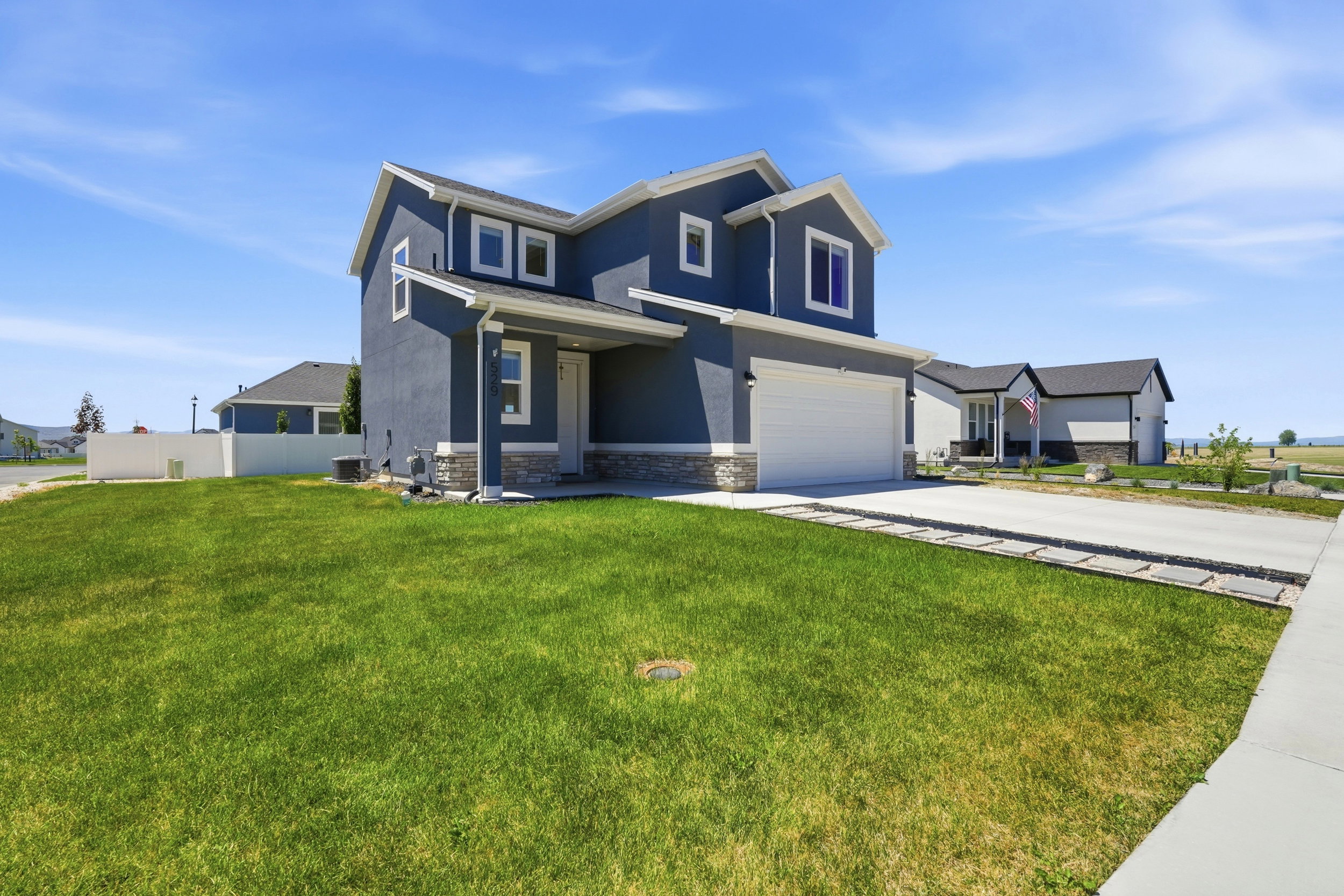 Two-story residence featuring a dark blue exterior with white trim, stone accent detailing, an attached garage, a concrete driveway, and a manicured lawn