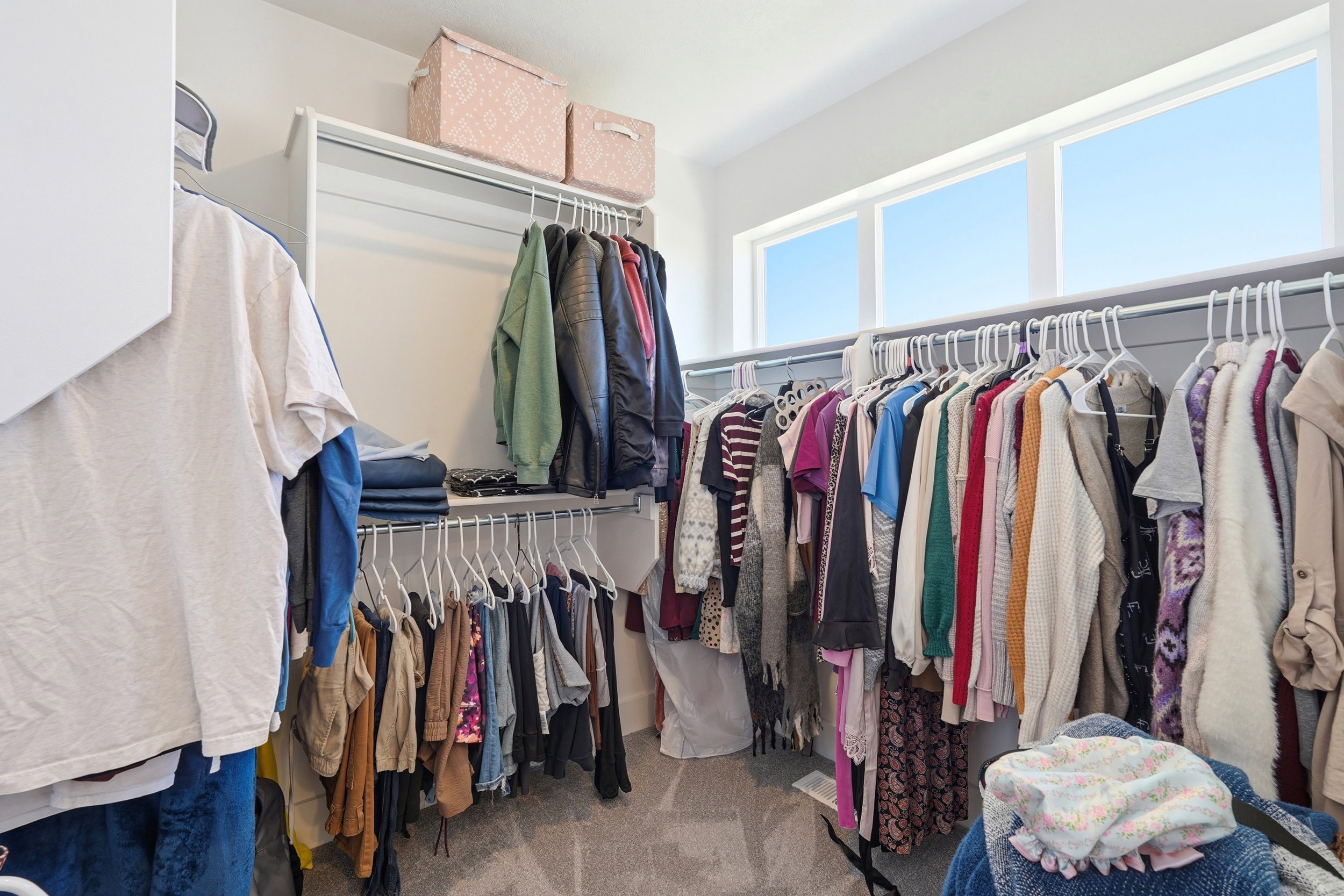Walk-in closet featuring built-in shelving, multiple hanging rods, and high transom windows providing natural light