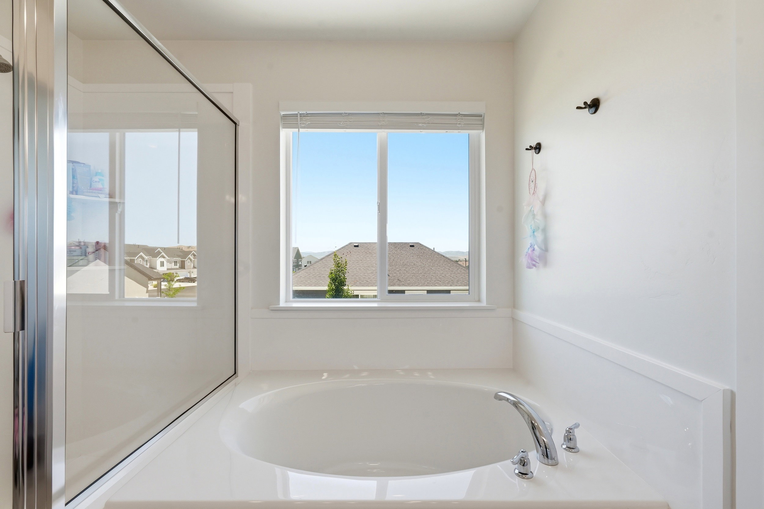 Built-in soaking tub with chrome fixtures, framed by a large window with neighborhood scenery