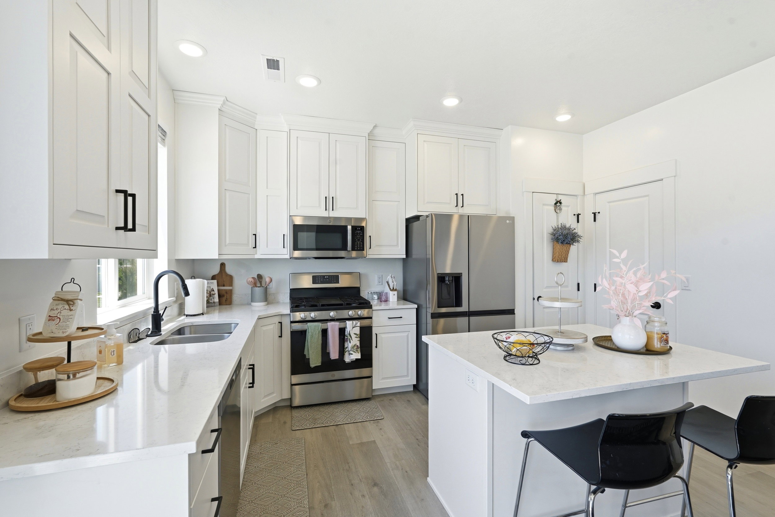 Kitchen featuring white cabinetry with matte black hardware, stainless steel appliances, light-toned countertops, and wood-finish flooring