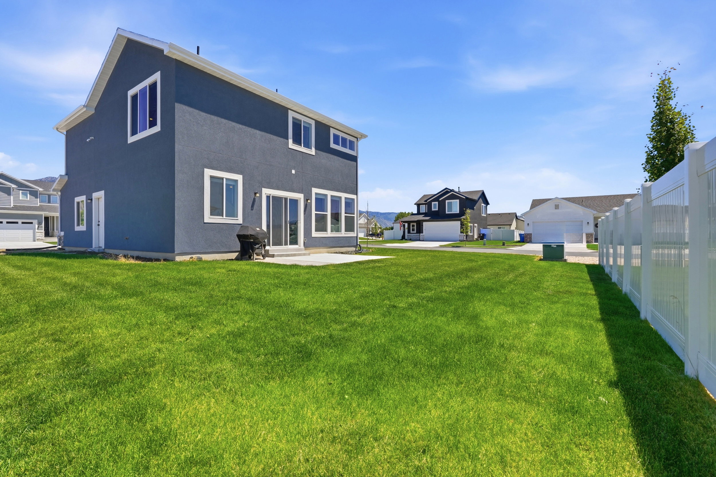 Expansive backyard featuring a manicured lawn, a concrete patio, a privacy fence, and a modern stucco exterior with white trim windows