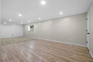 Spacious room featuring wood-finish flooring, recessed lighting, neutral paint, a window, and a white paneled door with black hardware