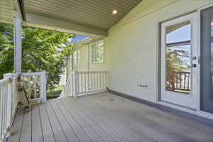 Covered deck with composite decking, white railing, recessed lighting, and direct access through a glass-paned door