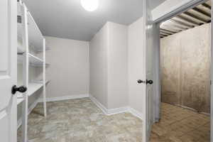 Storage room featuring white adjustable shelving, neutral-toned walls, and patterned tile flooring