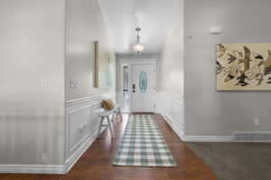 Entryway featuring wood-finish flooring, wainscoting, and a white paneled front door with decorative glass