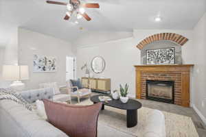 Living area featuring a brick fireplace with a wood mantel, vaulted ceiling, ceiling fan, and light gray flooring