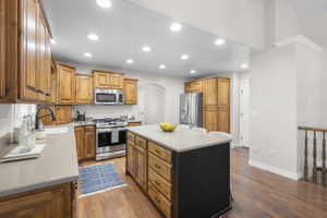 Kitchen featuring wood-finish cabinetry, stainless steel appliances, a center island with a black beadboard base, light-colored countertops, and recessed lighting