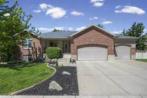 Brick exterior residence with a dual garage featuring arched openings, a concrete driveway, and a landscaped front yard