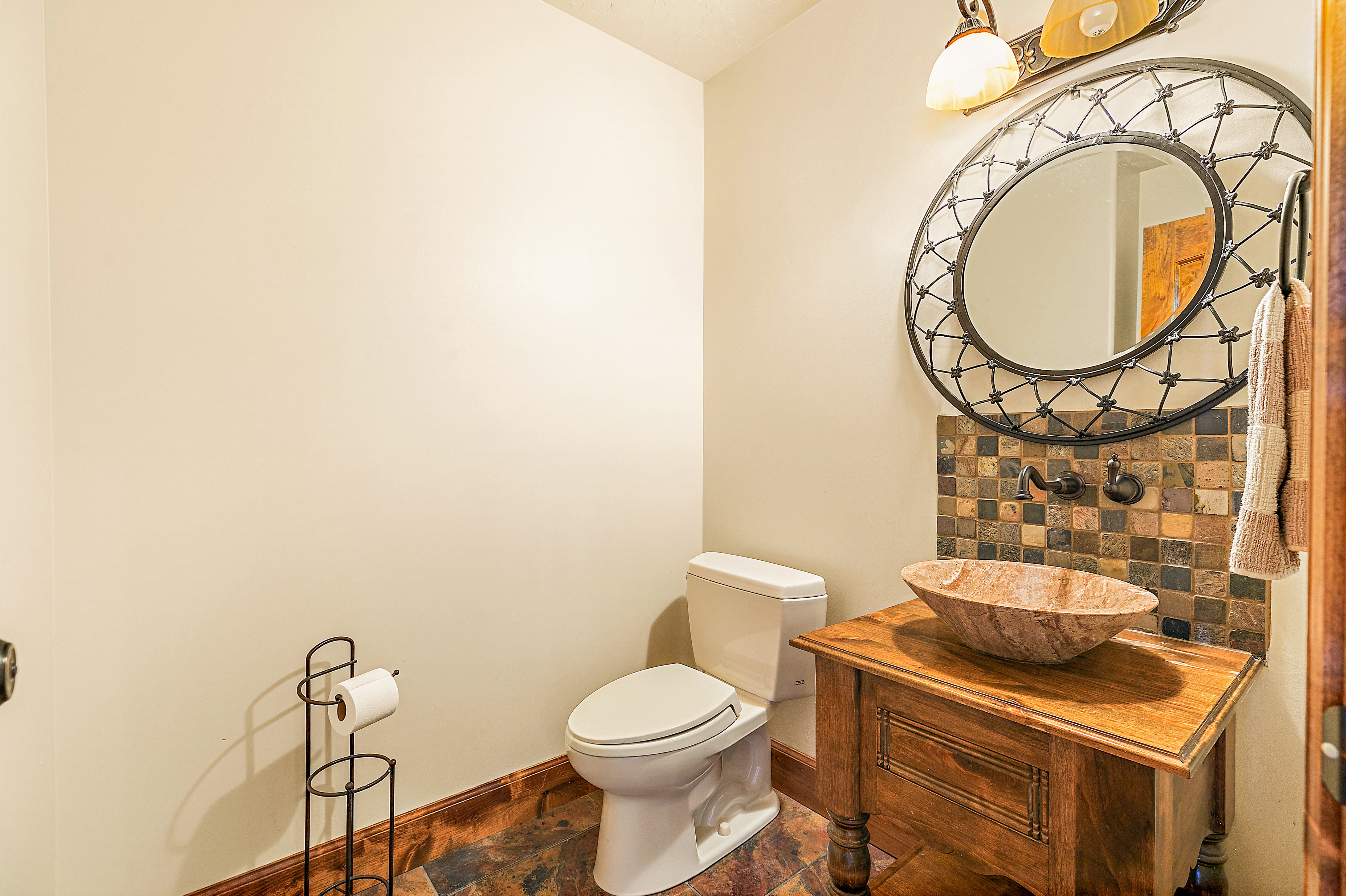 Powder room featuring a unique vessel sink, a mosaic tile backsplash, a decorative wall mirror, and a wood-finish vanity