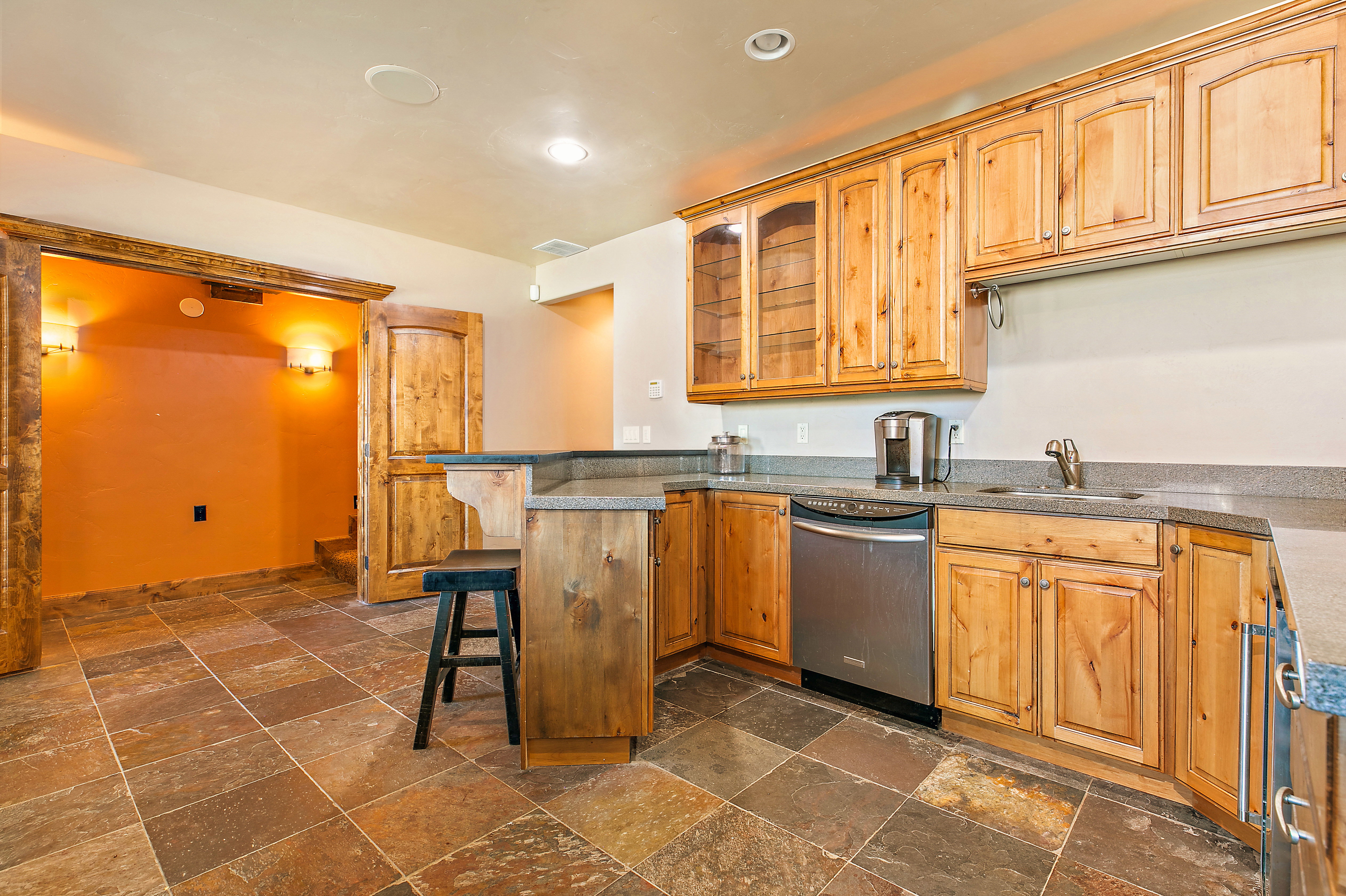 Built-in wet bar featuring stone tile flooring, knotty wood cabinetry, stone countertops, a stainless steel dishwasher, and a bar seating area