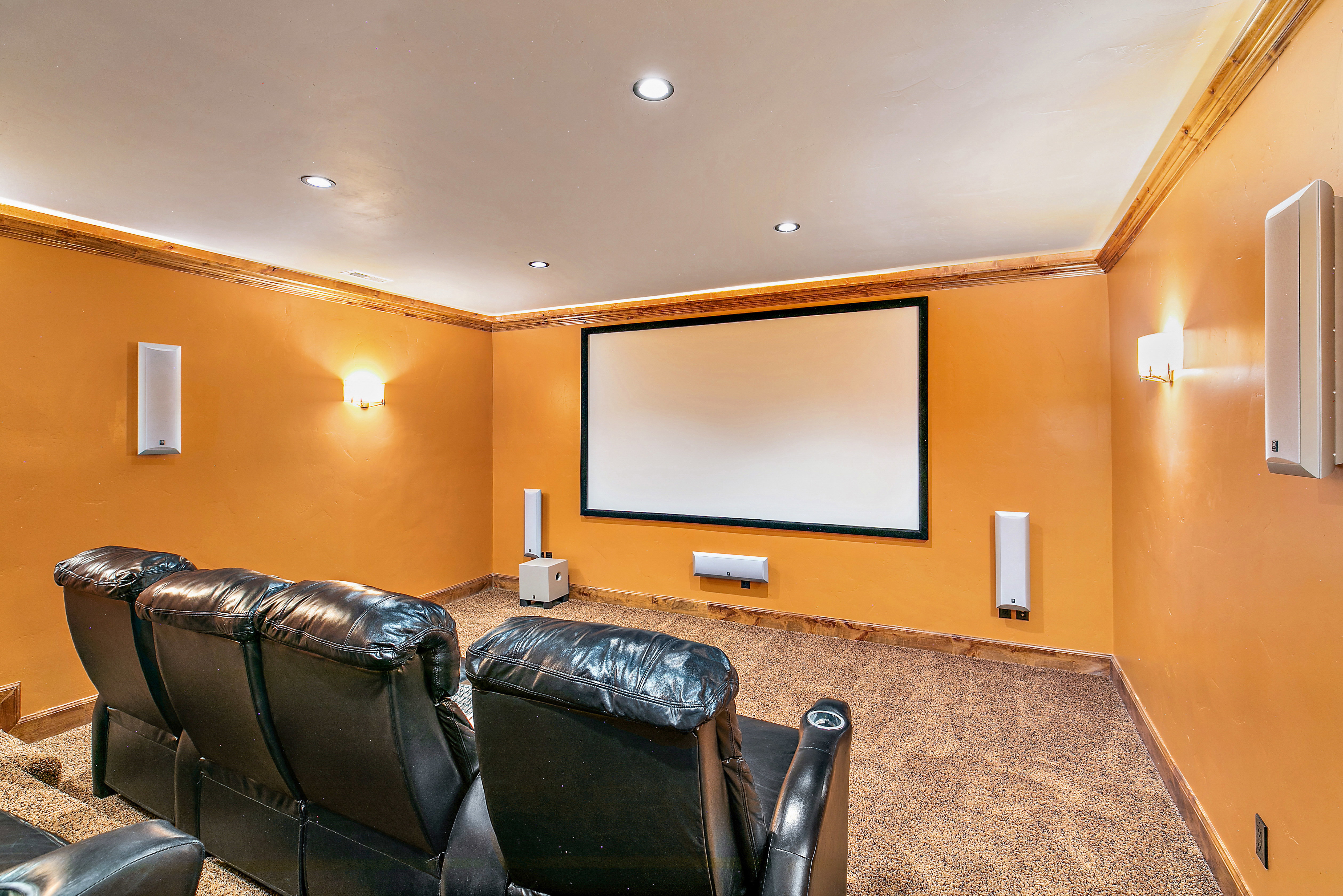 Dedicated media room featuring a large projection screen, recessed lighting, wall sconces, and crown molding