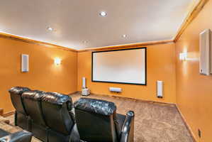 Dedicated media room featuring a large projection screen, recessed lighting, wall sconces, and crown molding