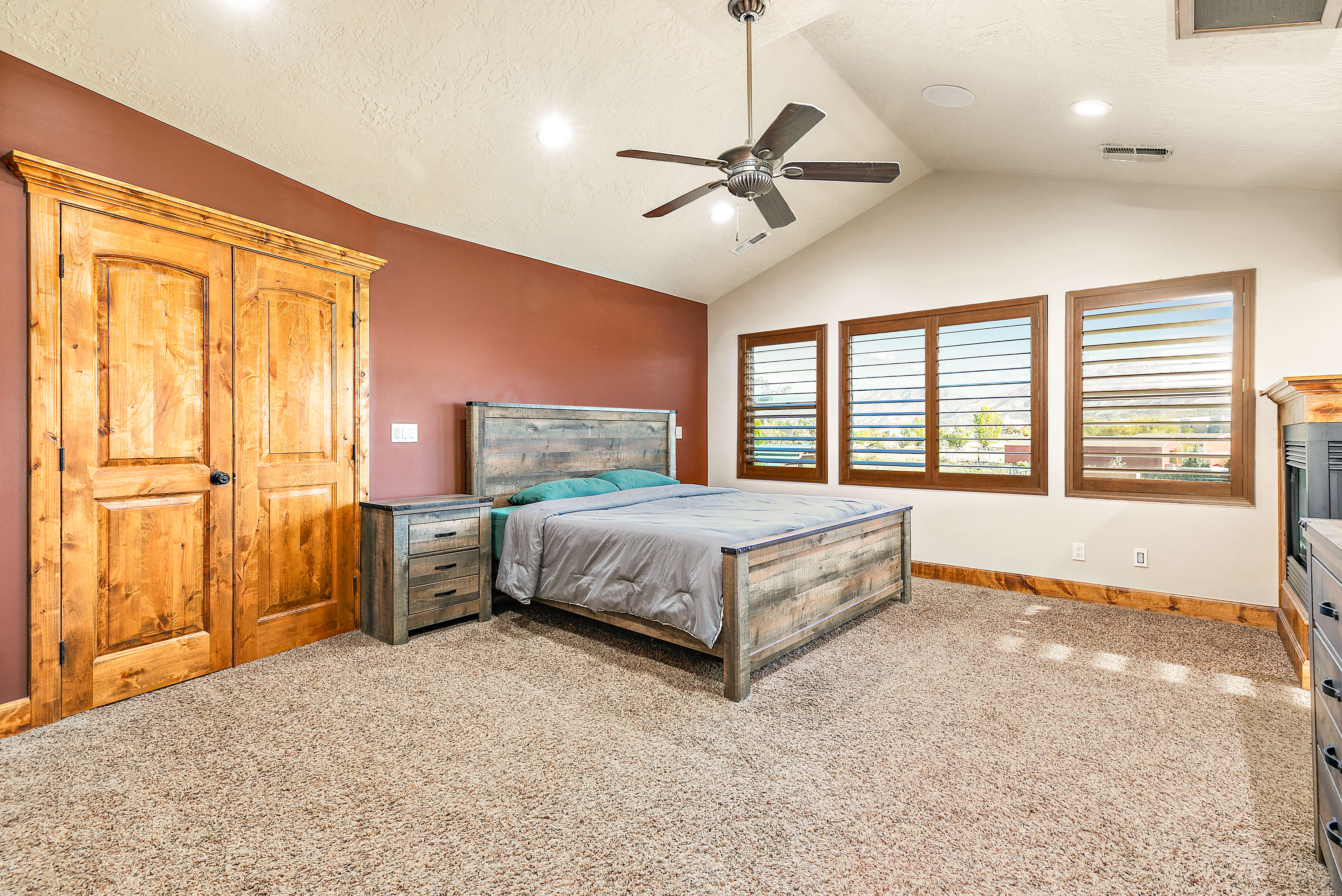 Vaulted ceilings with a ceiling fan, three windows with wood shutters, recessed lighting, and a neutral carpeted floor