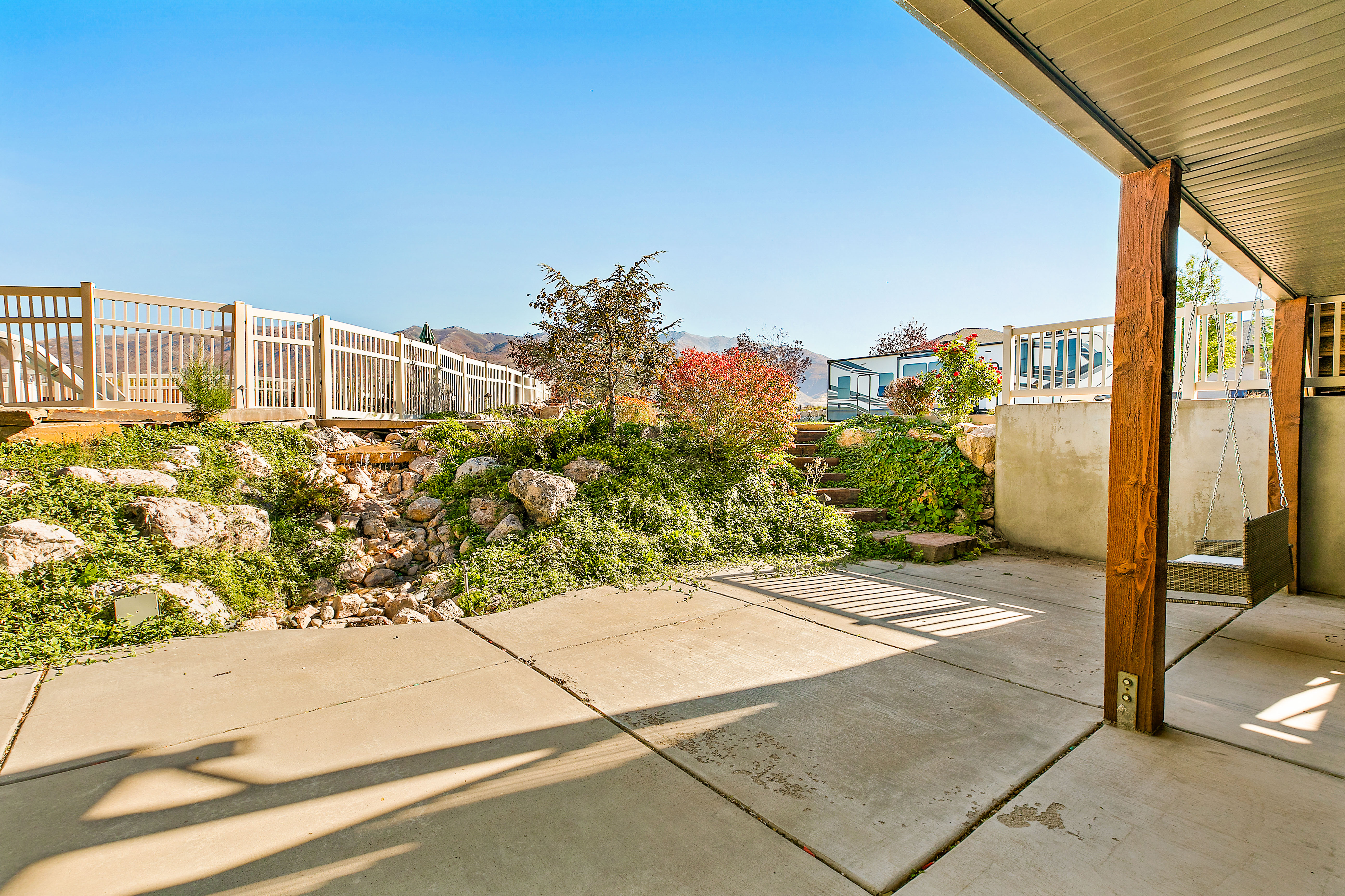 Concrete patio with an exposed wood beam structure, featuring a terraced hillside with rock accents and integrated steps
