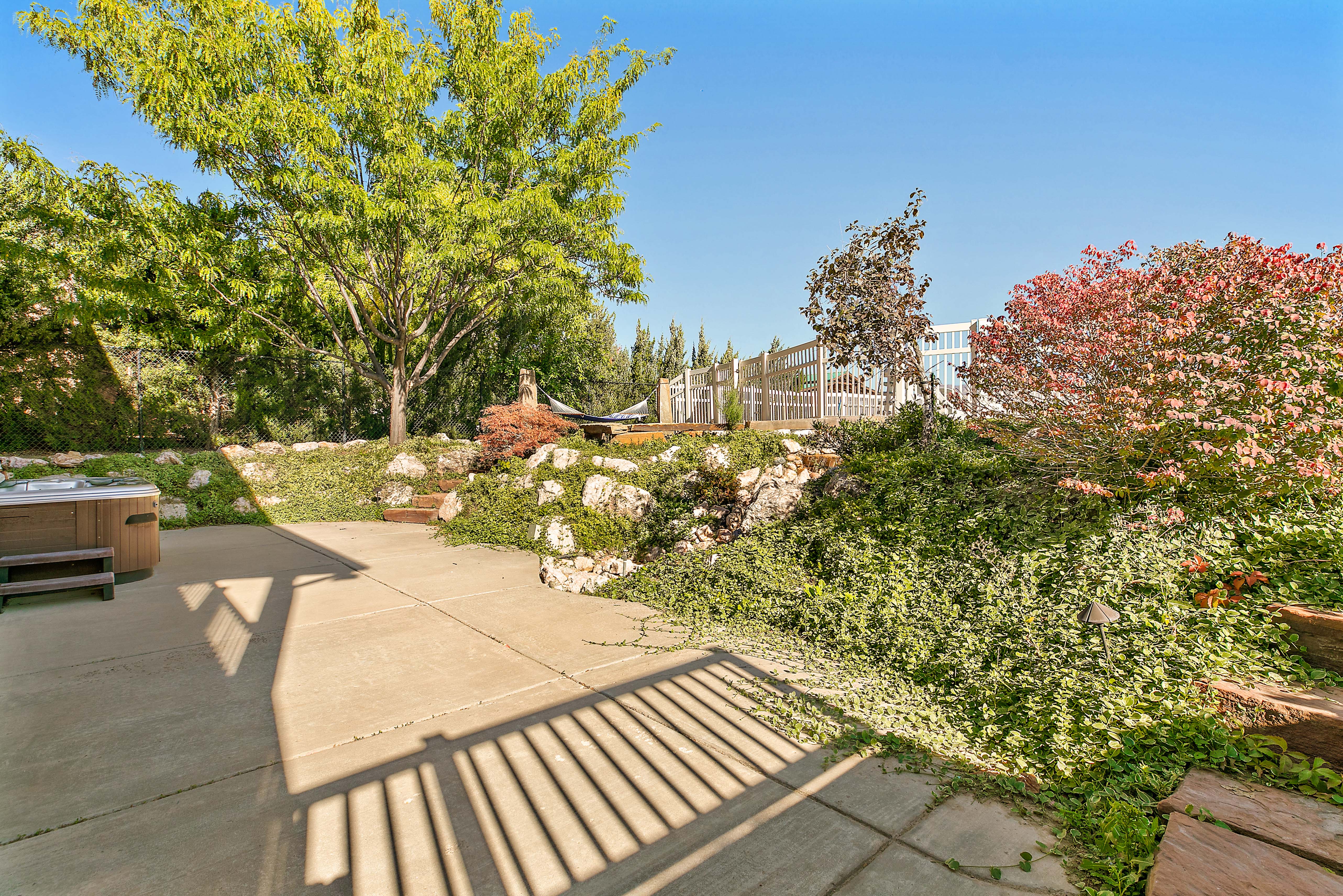 Patio area with a built-in hot tub, concrete paving, and a sloped landscape with integrated rockery and diverse plantings
