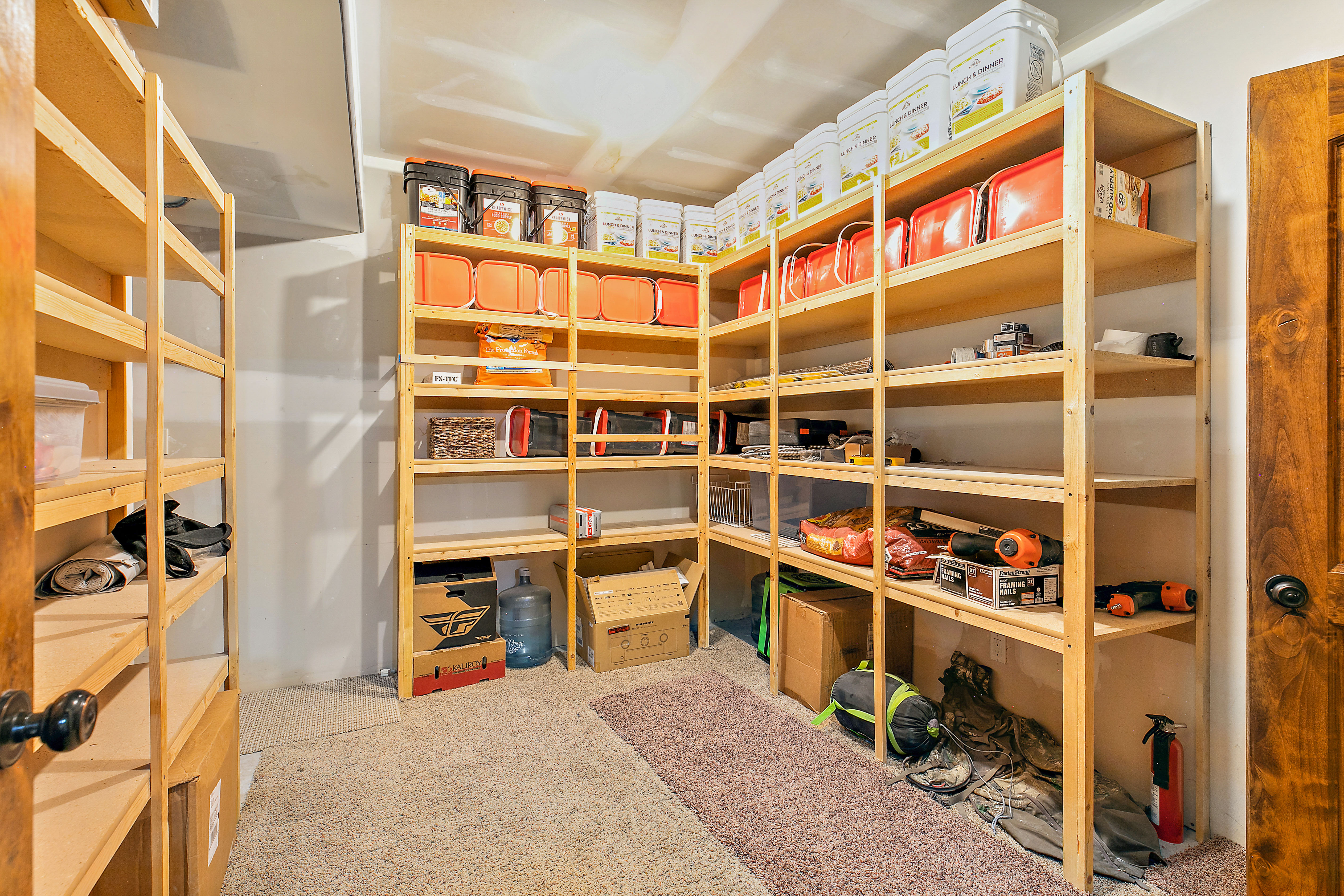 Spacious storage area featuring extensive built-in wooden shelving, neutral-toned walls, and soft carpet flooring