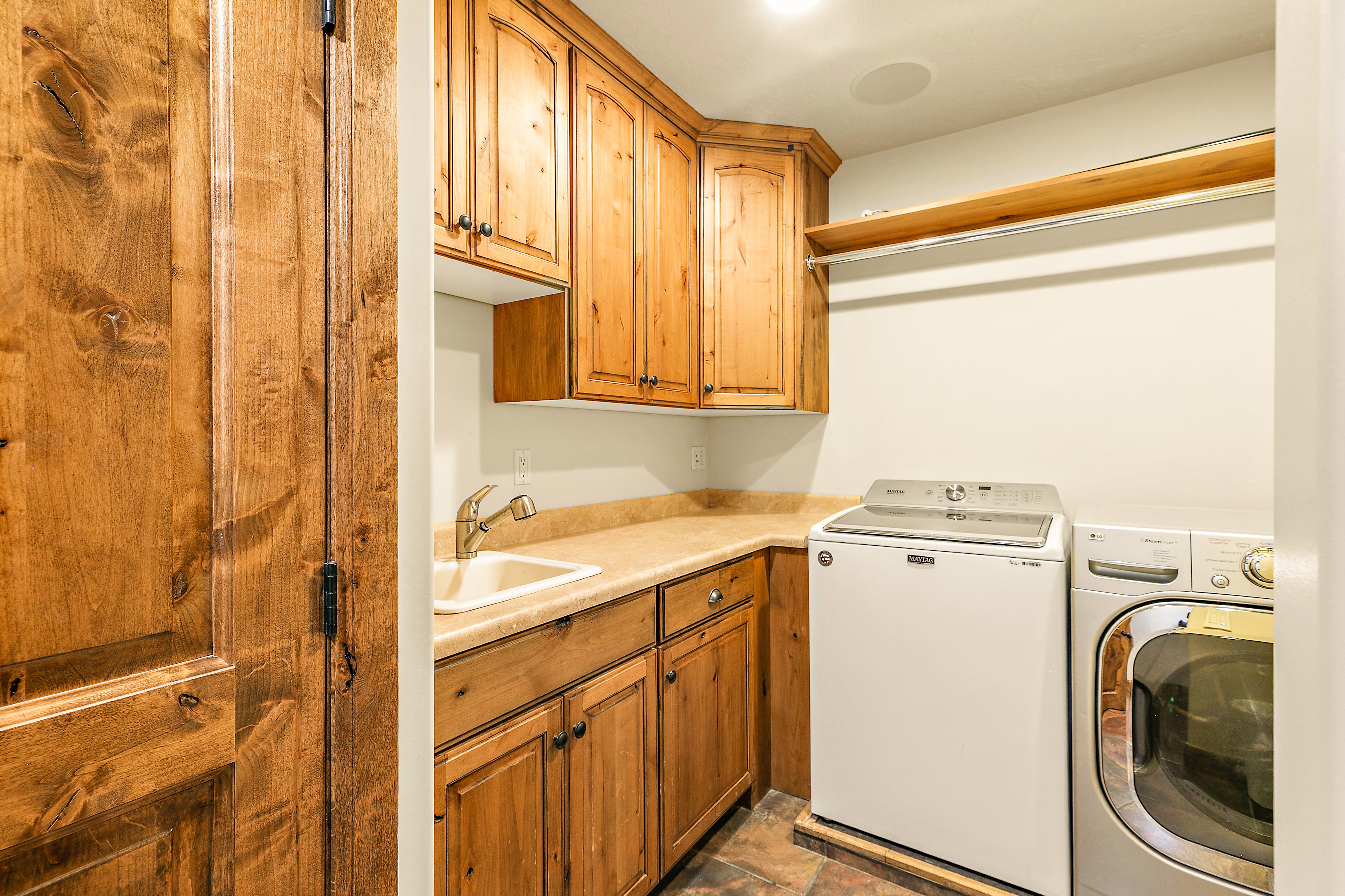 Utility room featuring natural wood cabinetry, a beige countertop with an integrated sink, a hanging rod with a shelf, and tiled flooring