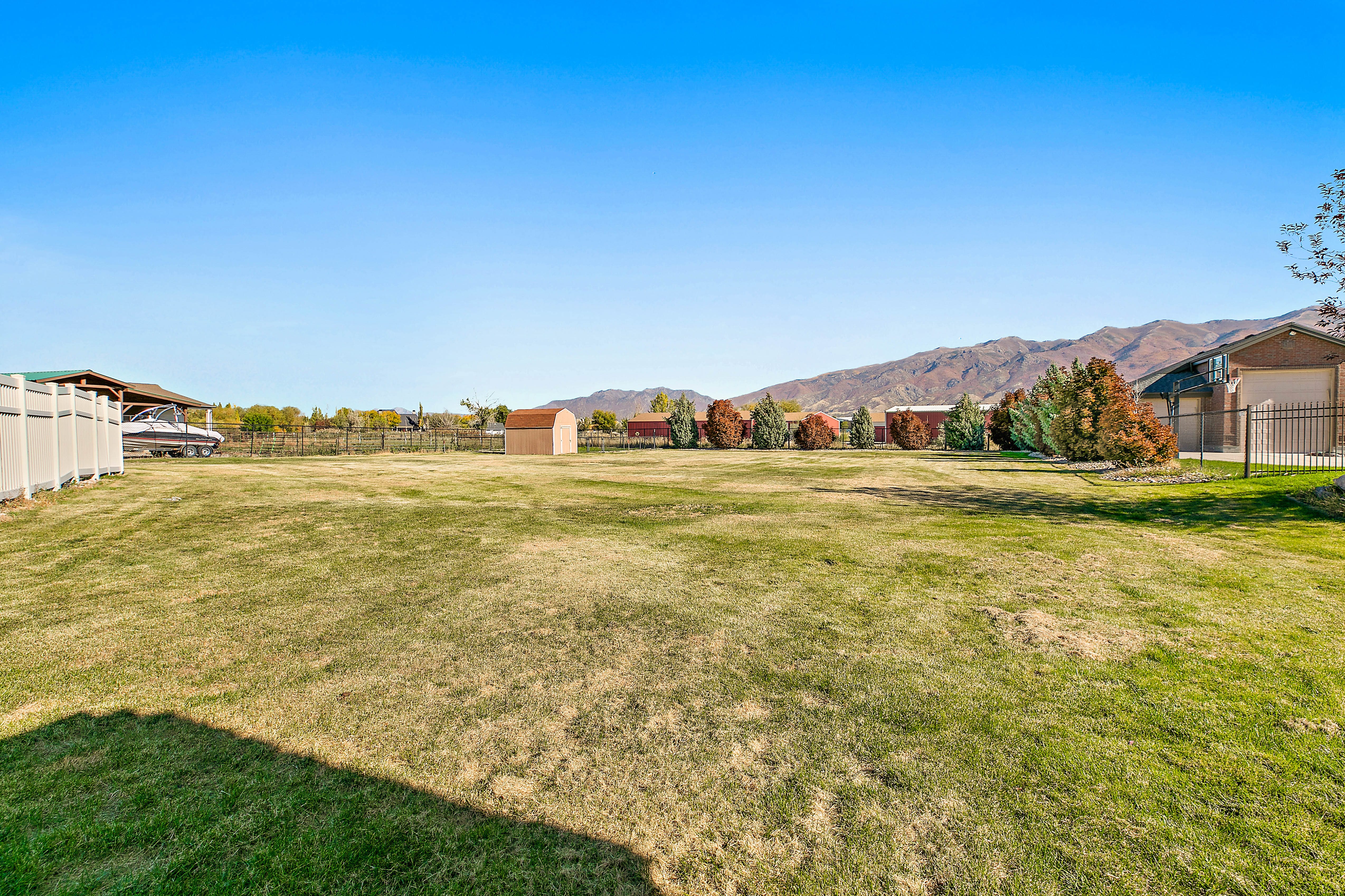 Expansive grassy lot featuring a distant mountain backdrop, a storage shed, and mature trees lining the perimeter