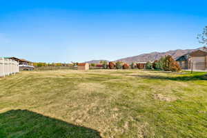 Expansive grassy lot featuring a distant mountain backdrop, a storage shed, and mature trees lining the perimeter