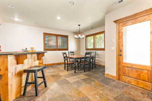 Spacious recreation area featuring multi-toned slate tile flooring, a wood-paneled bar, wood plantation shutters, and a wood entry door with opaque glass